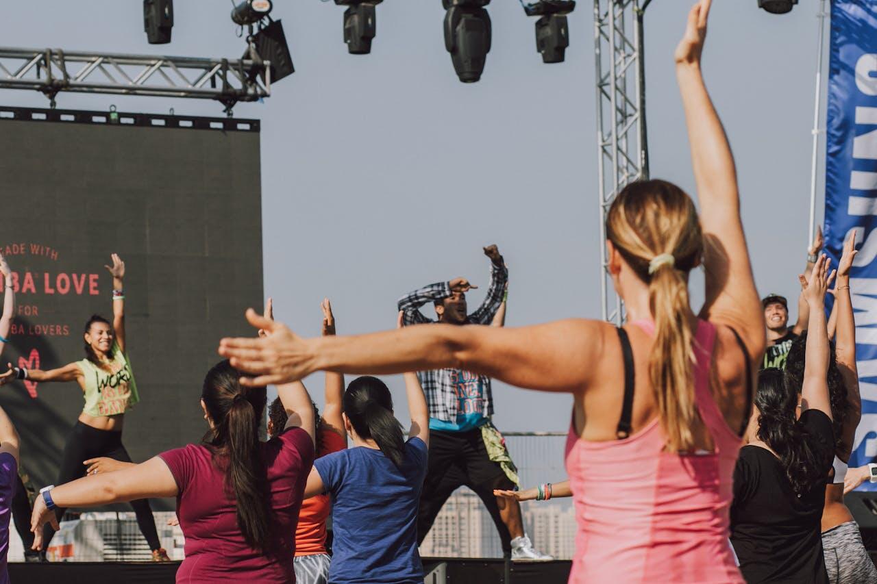 A group of dancers enthusiastically following a leader on stage during a vibrant outdoor dance event.