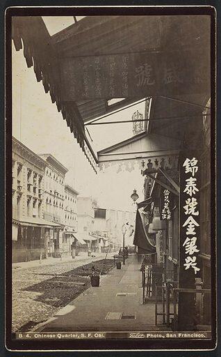 An old photo of a street featuring Asian writing on signs and buildings, capturing a historical urban scene.