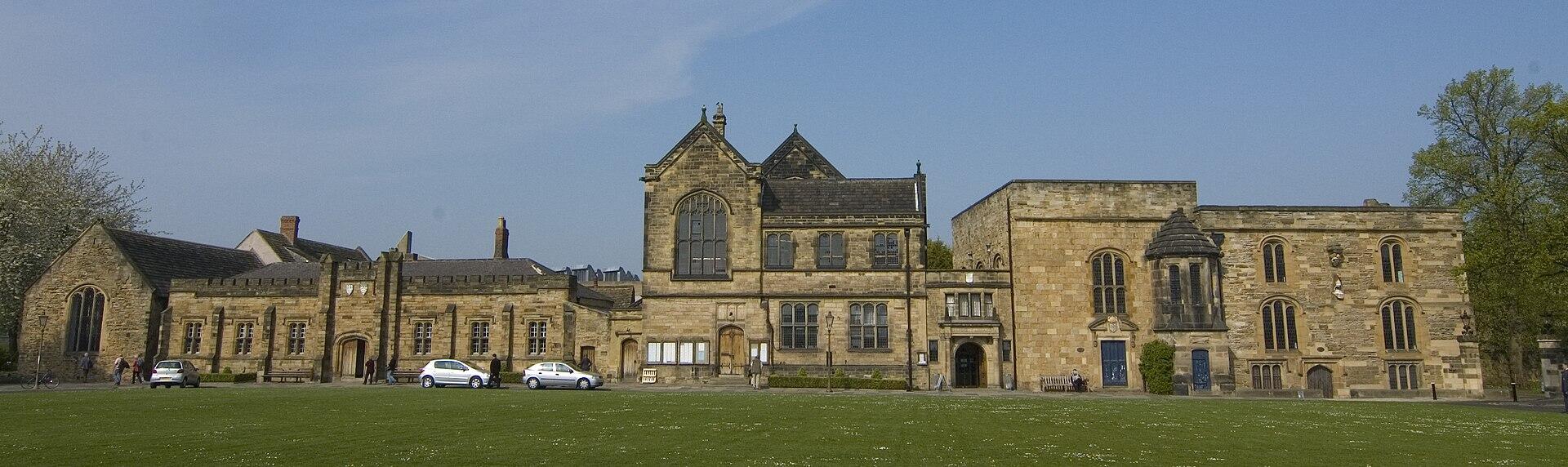 A long stone building behind a lawn on a sunny day.