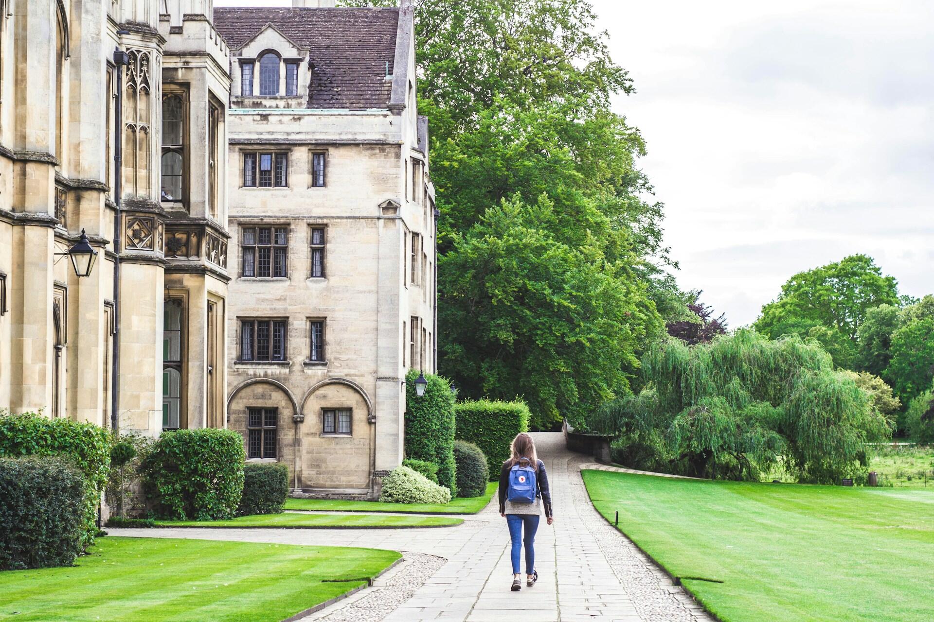 A person with a backpack walks a path in front of a building. 