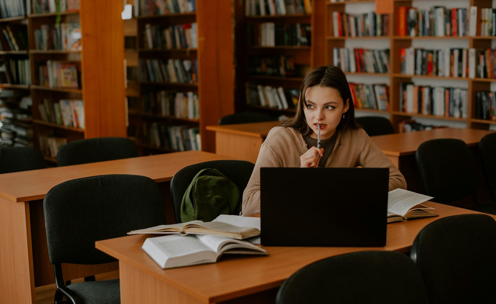 female student working in a library looking pensively into the distance while working on a computer