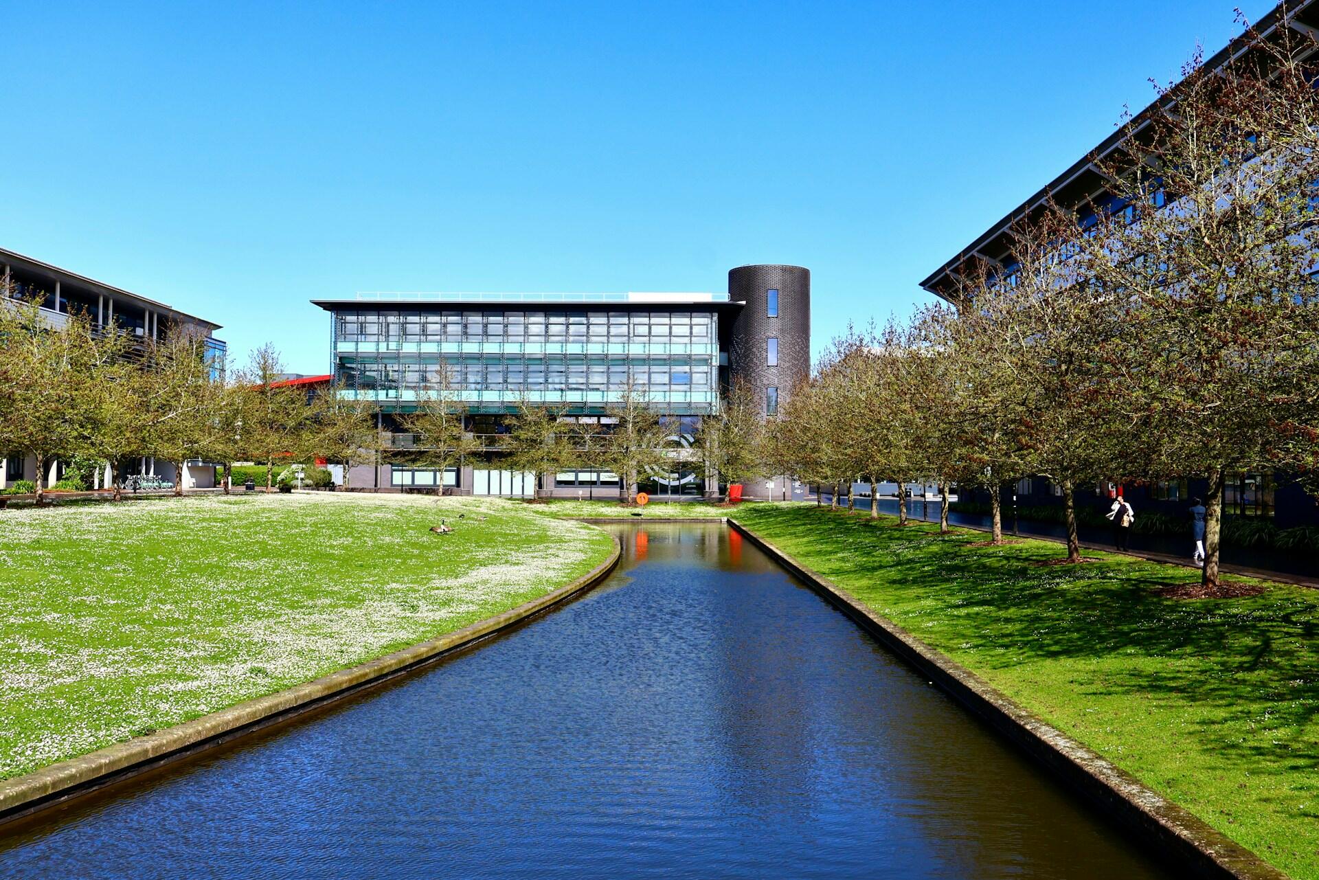 A modern building behind a greenspace and waterway. 