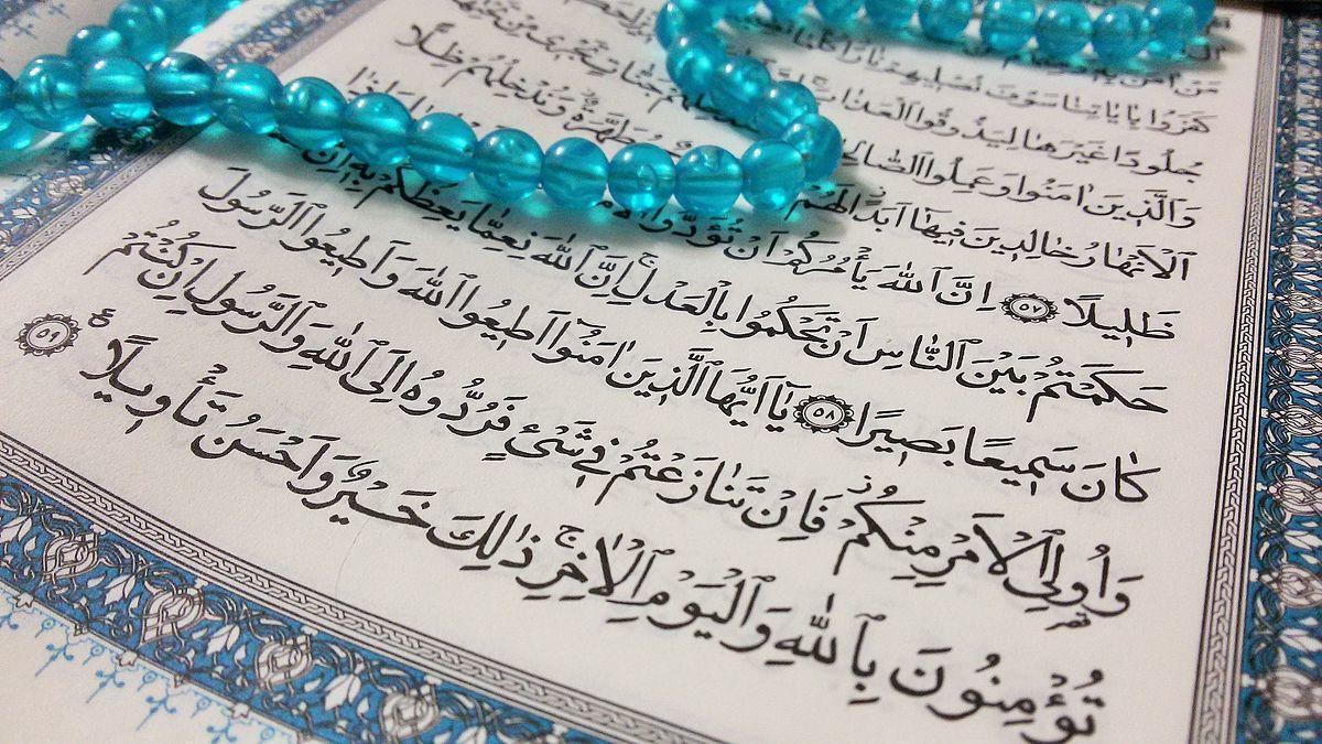 arabic writing in a book with blue beads laying over the book