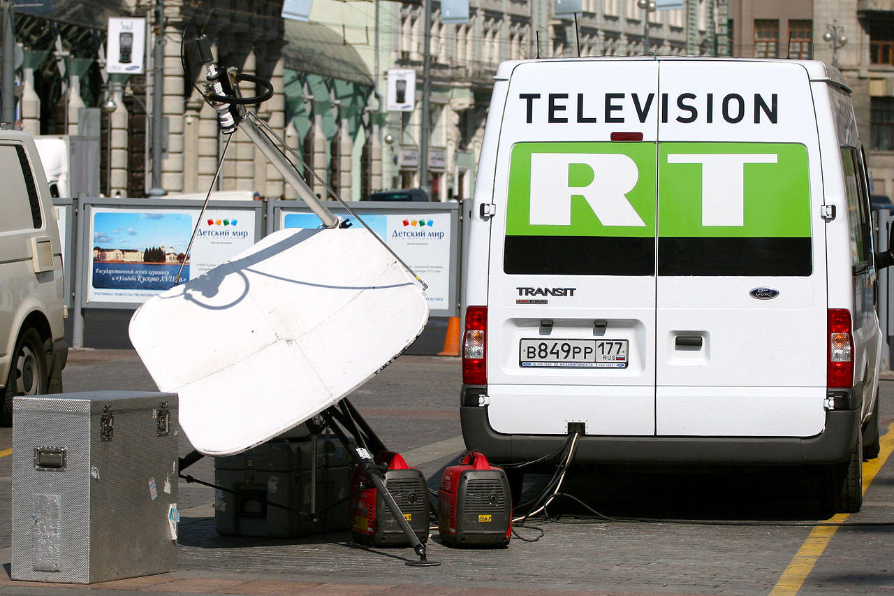a white van with 'television RT' written on it parked at a gas station
