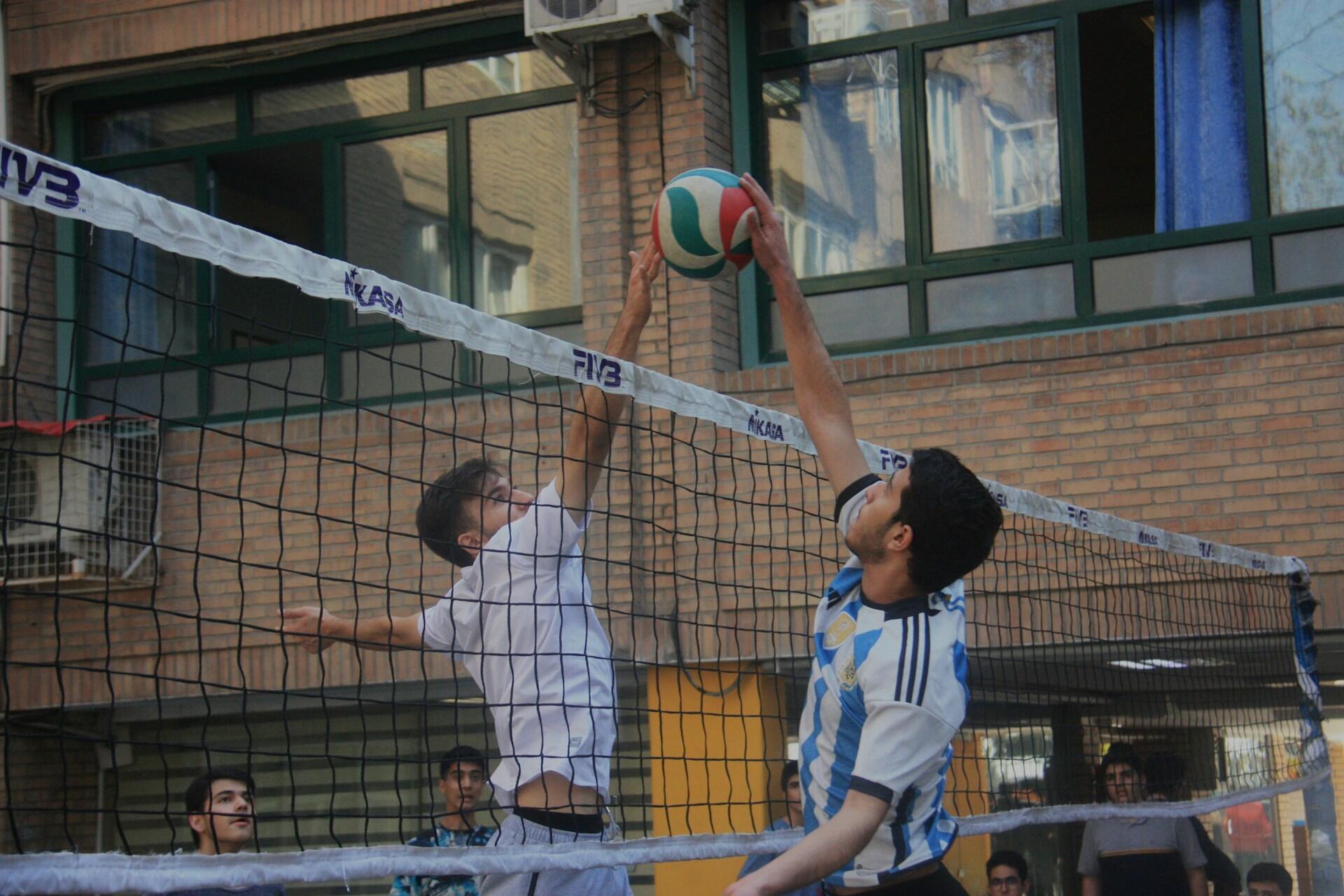 A casual volleyball game, where two players are blocking the ball.