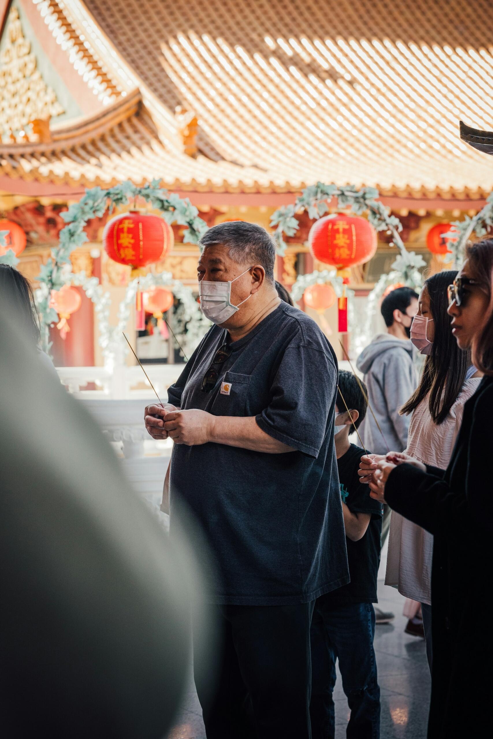 A group of people gathered in a vibrant temple, holding incense sticks and lanterns, celebrating a cultural ritual in a festive atmosphere.
