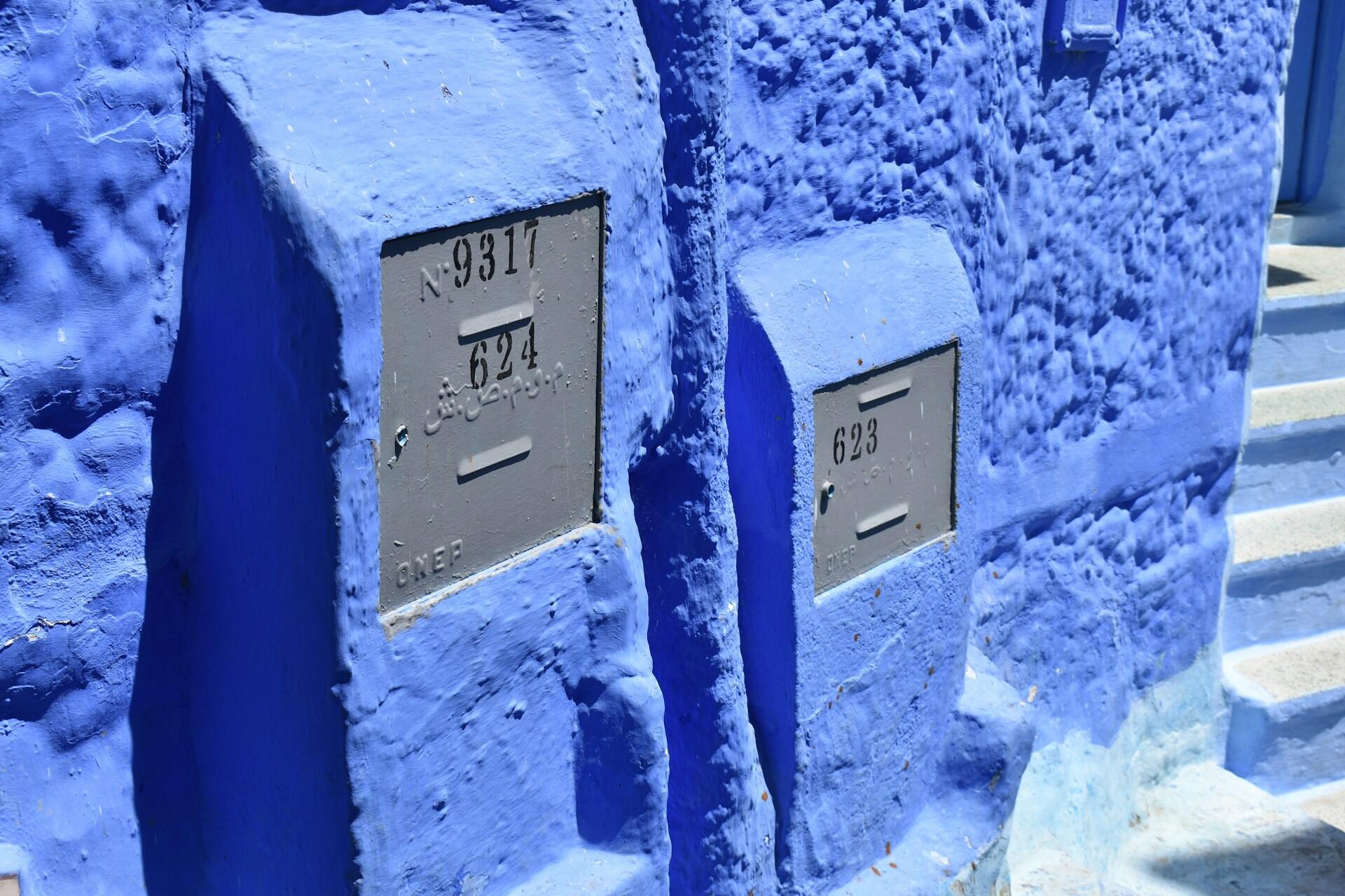 Two blue-painted stone mailboxes with gray metal covers numbered 9317-624 and 623 embedded in a textured blue wall near blue stairs.