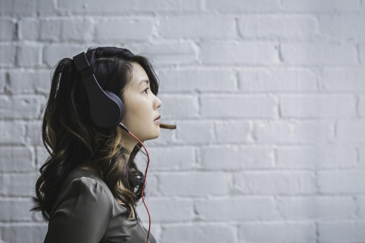 a woman with a headset on looking into the distance in front of a white brick wall