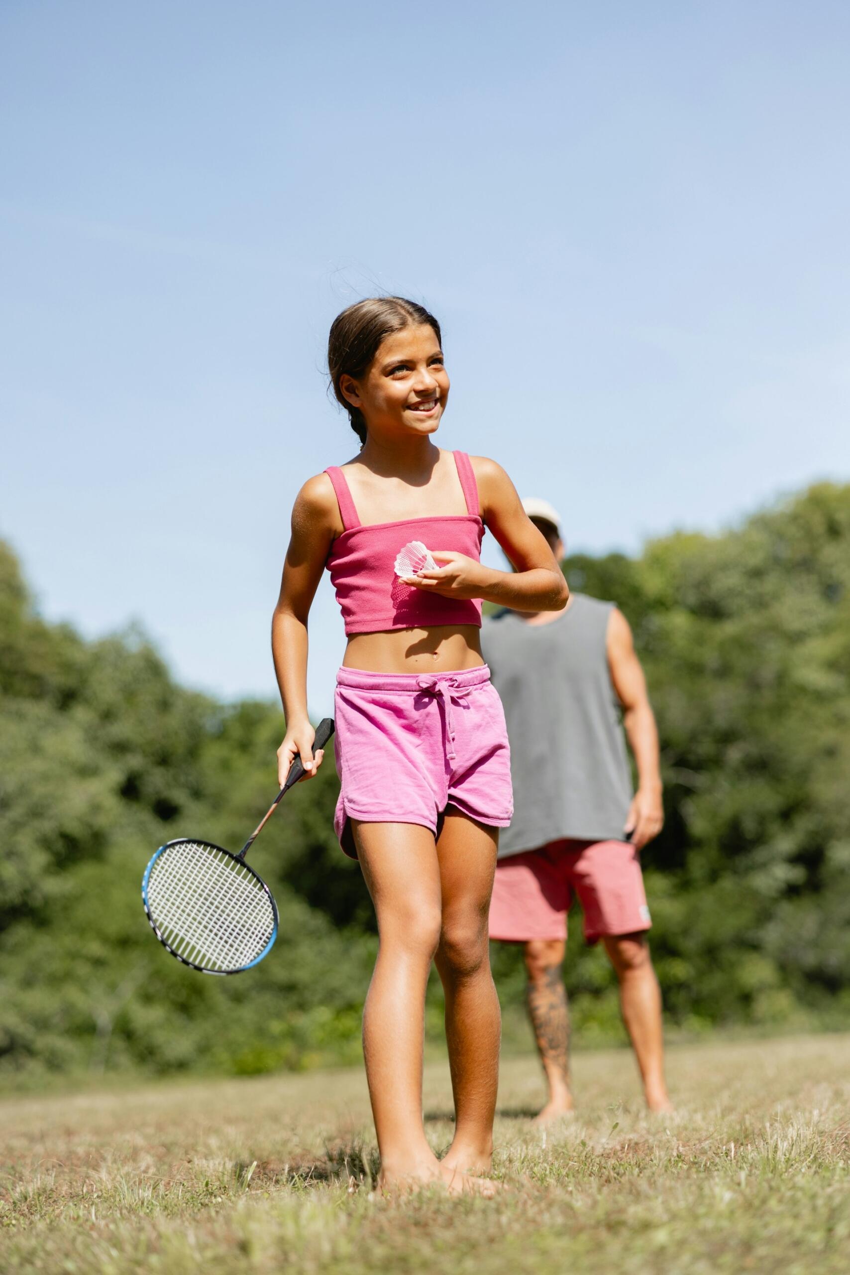 A girl wearing pink holds a badminton racket and birdie. 