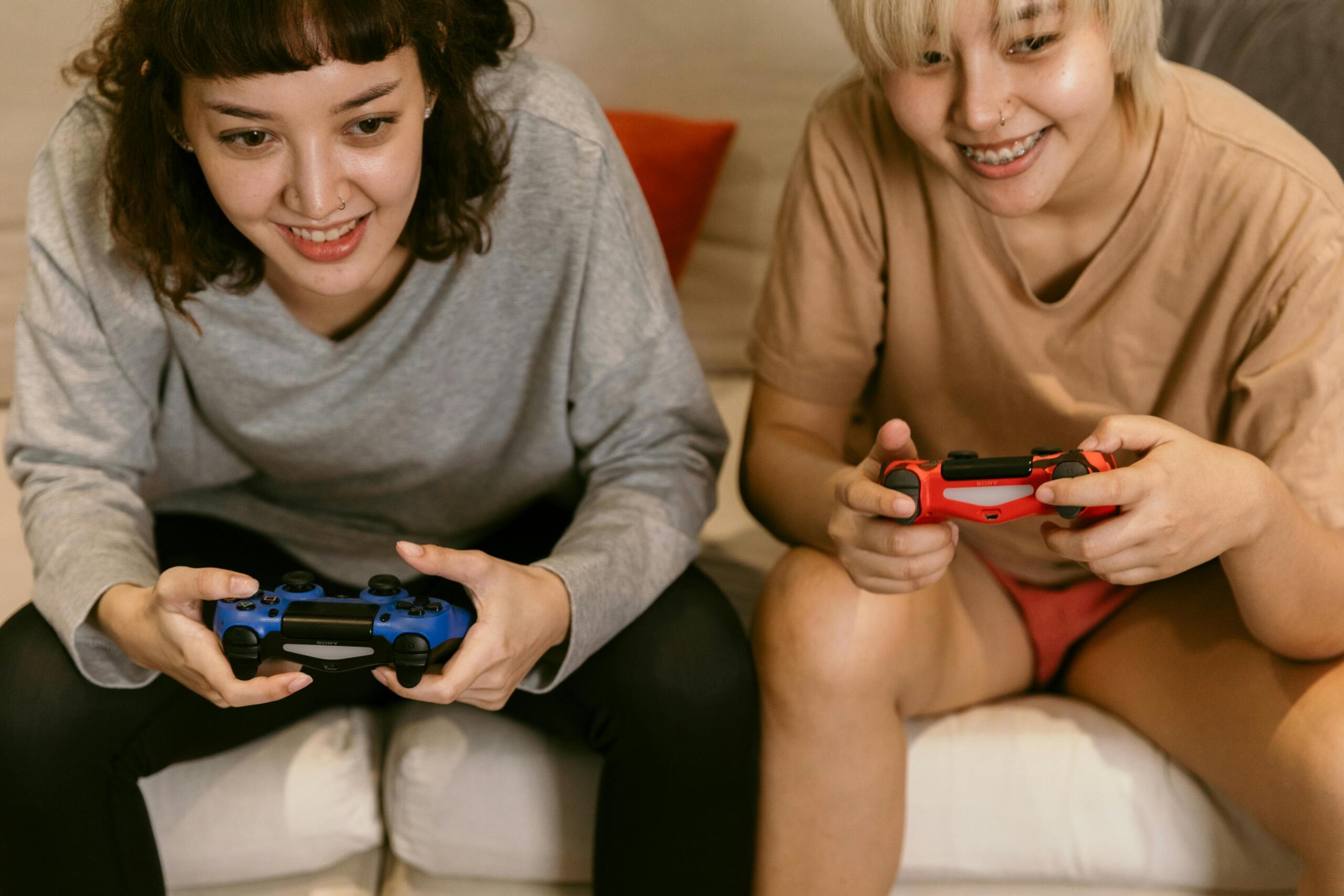 Two women sitting side by side, focused and smiling as they play video games with controllers in hand.