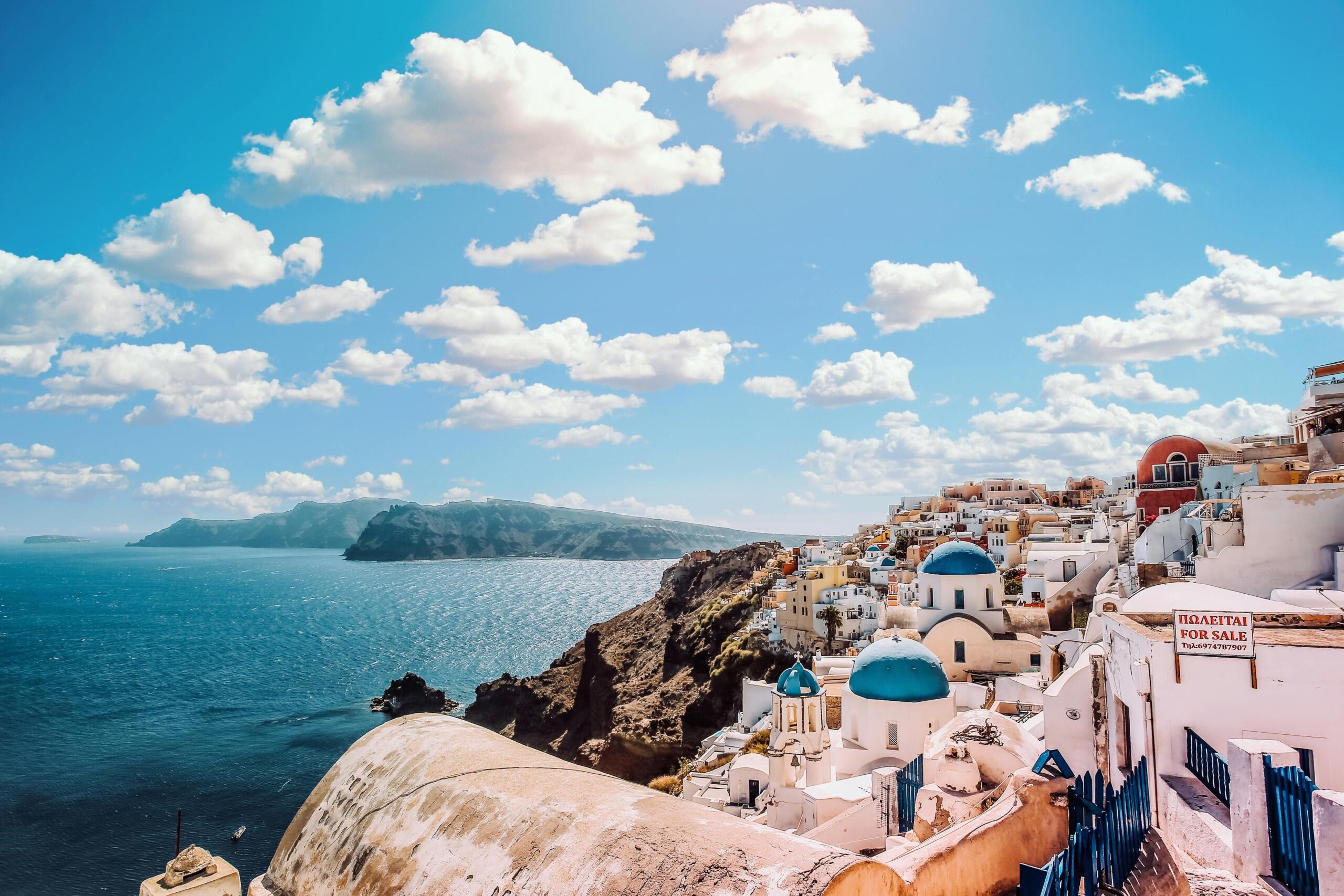 Scenic view of a traditional Greek town with whitewashed buildings and terracotta roofs overlooking the blue waters of the Aegean Sea.