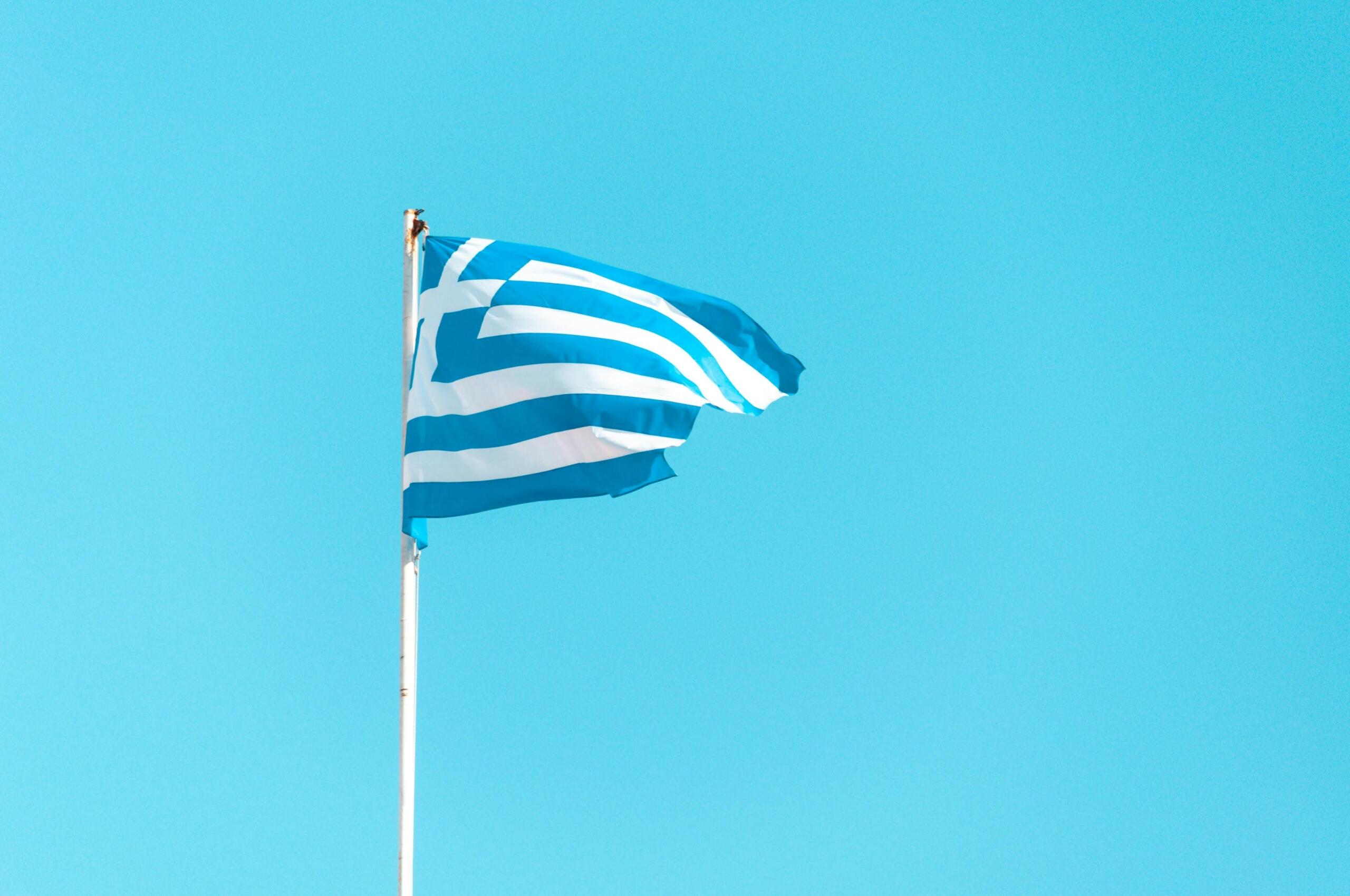 Greek flag waving in the wind against a clear blue sky.