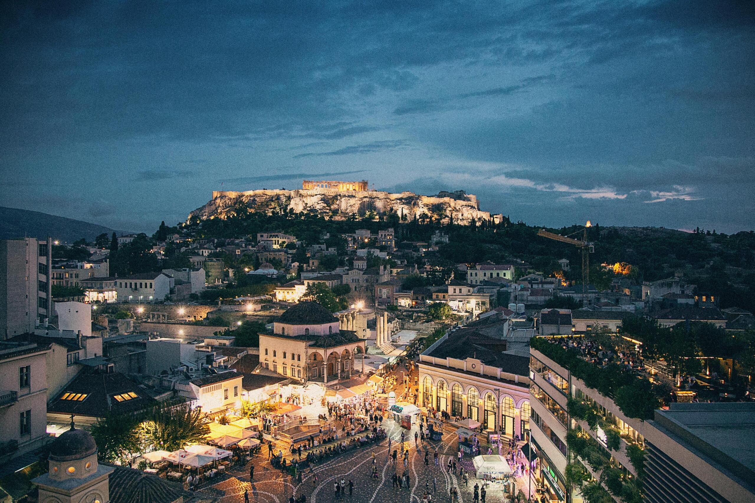 Night view of the Parthenon illuminated on the Acropolis hill, with the city lights of Athens glowing in the foreground.