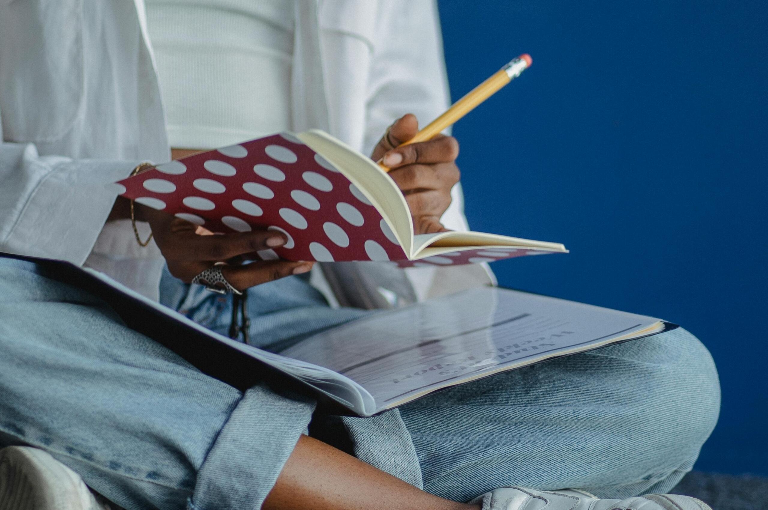 Person writing in a notebook while holding an open textbook on their lap, focused on studying.