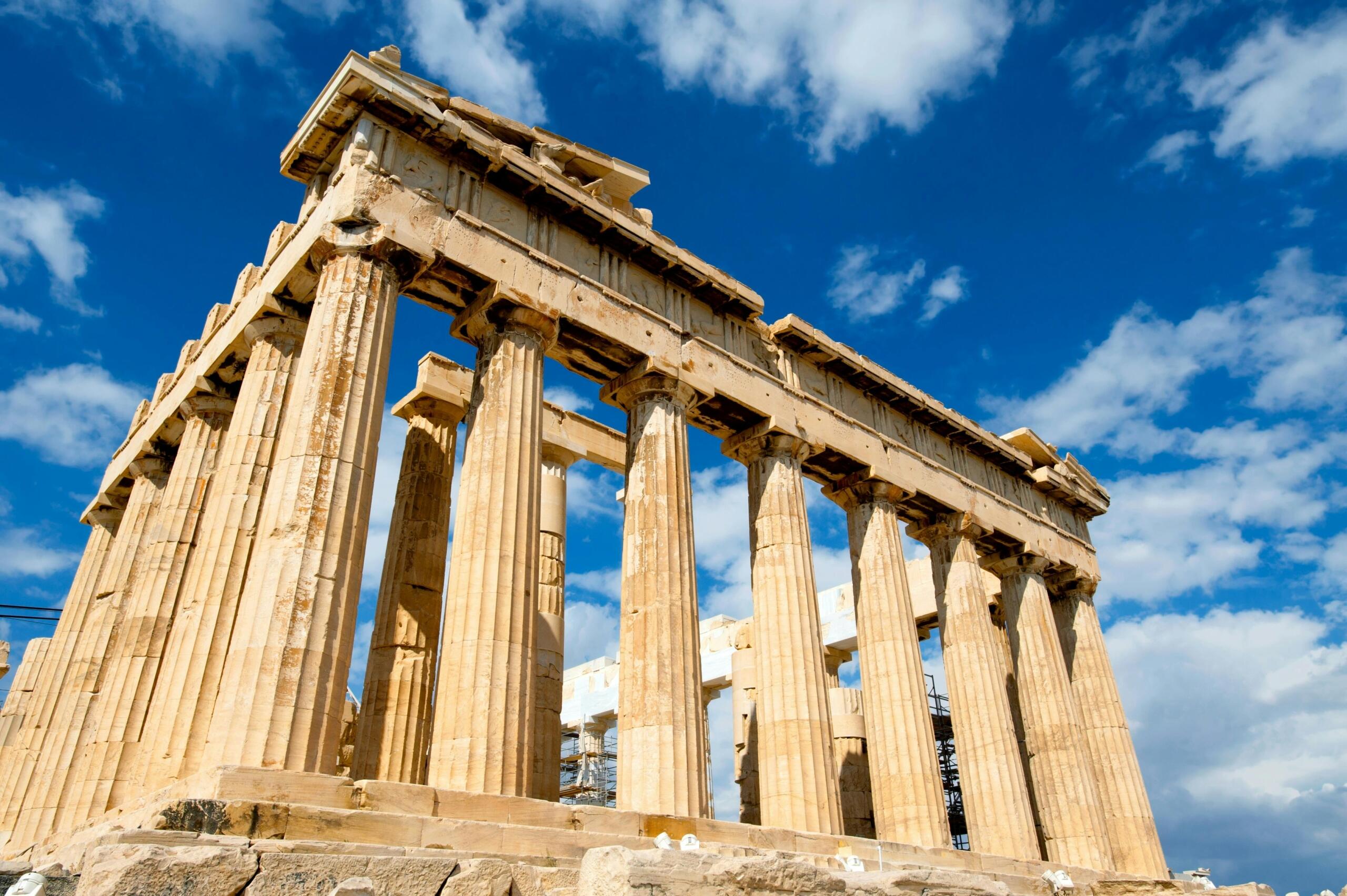 Photo of ancient Greek pillars made of weathered stone, standing tall against a clear blue sky.
