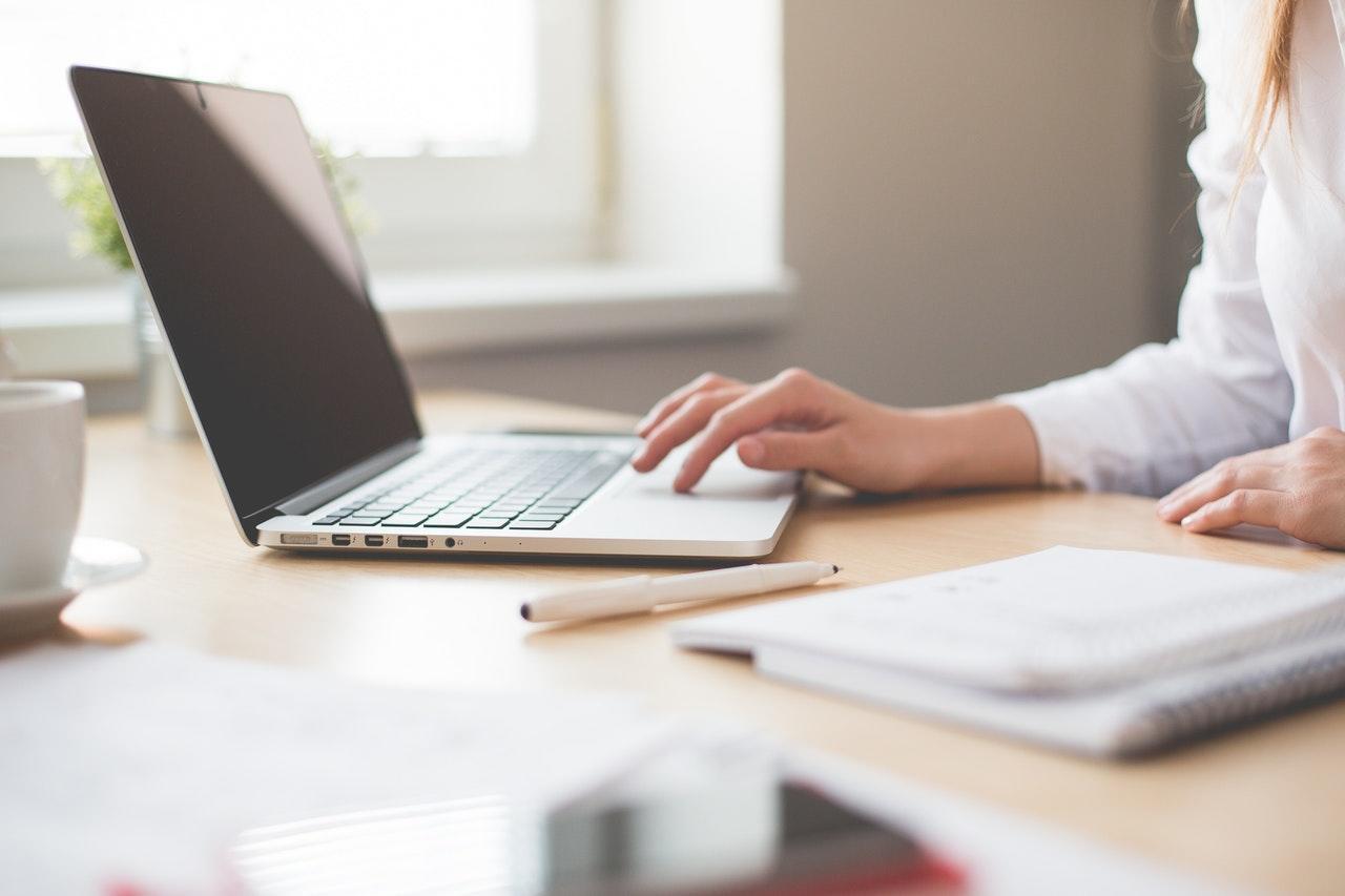 woman working on a computer at a desk with an notebook