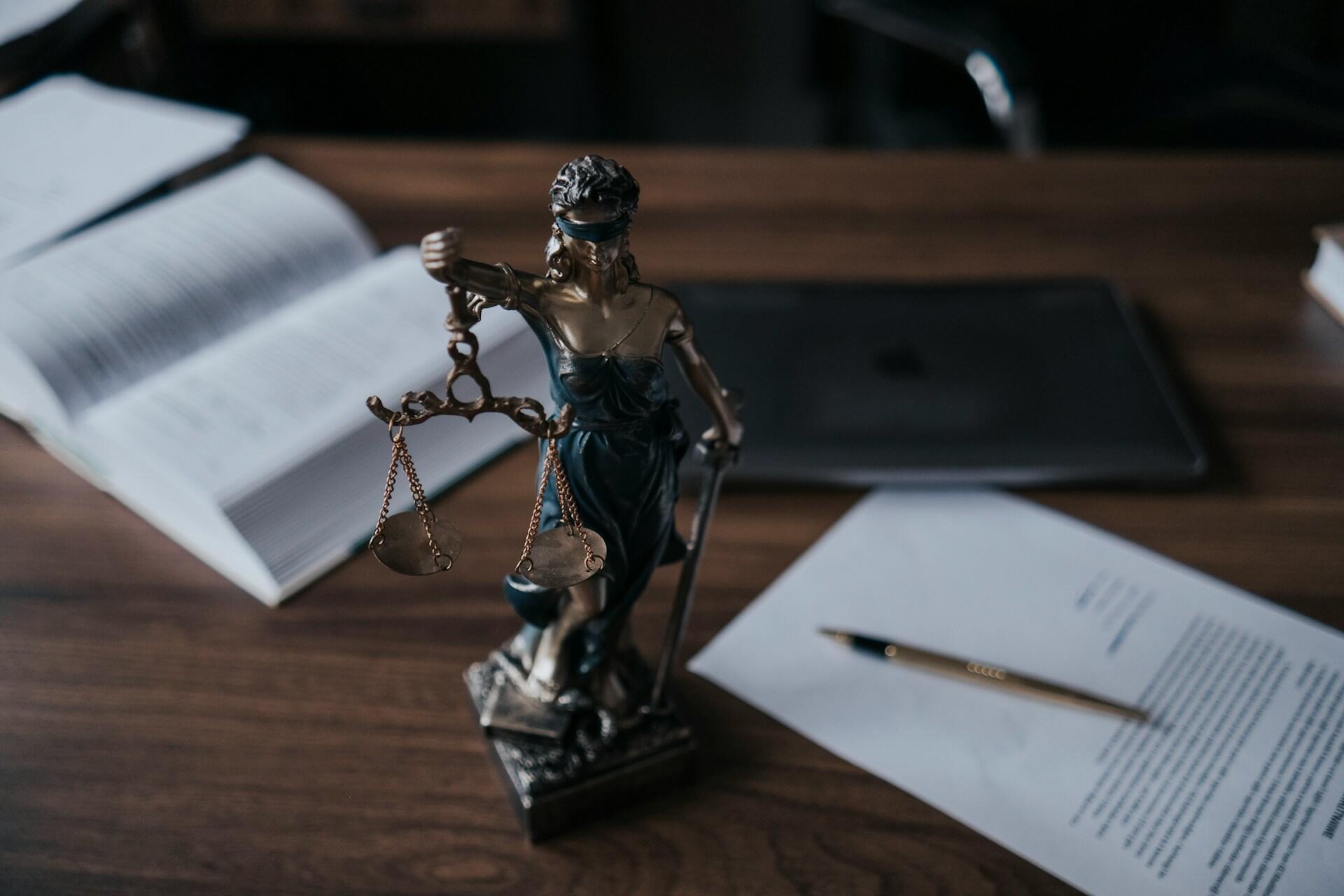 A statue of Lady Justice, blindfolded and holding scales, displayed on a lawyer's desk.