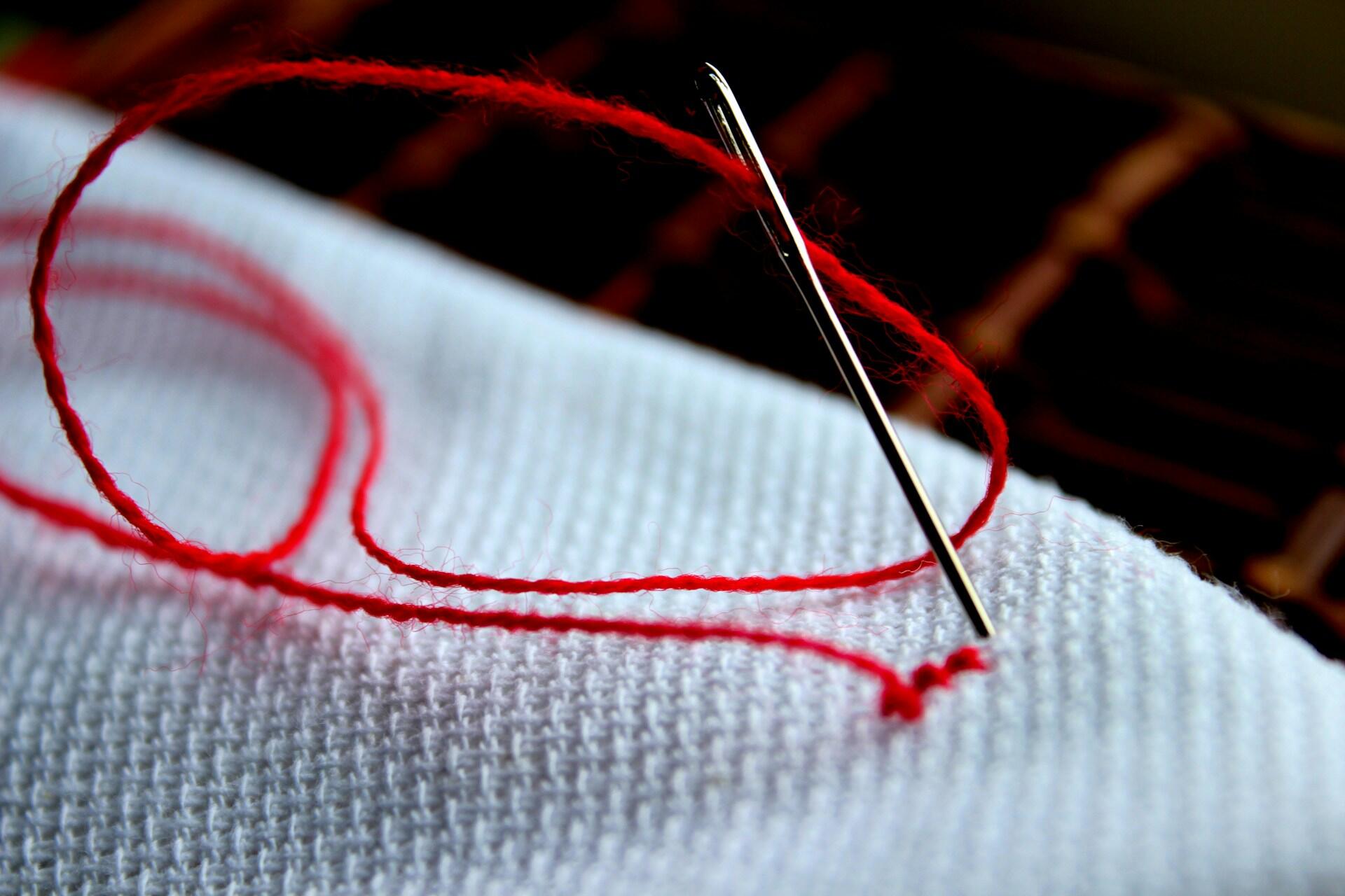 A close-up of a sewing needle threaded with red yarn lying on textured white fabric, showcasing the art of embroidery.