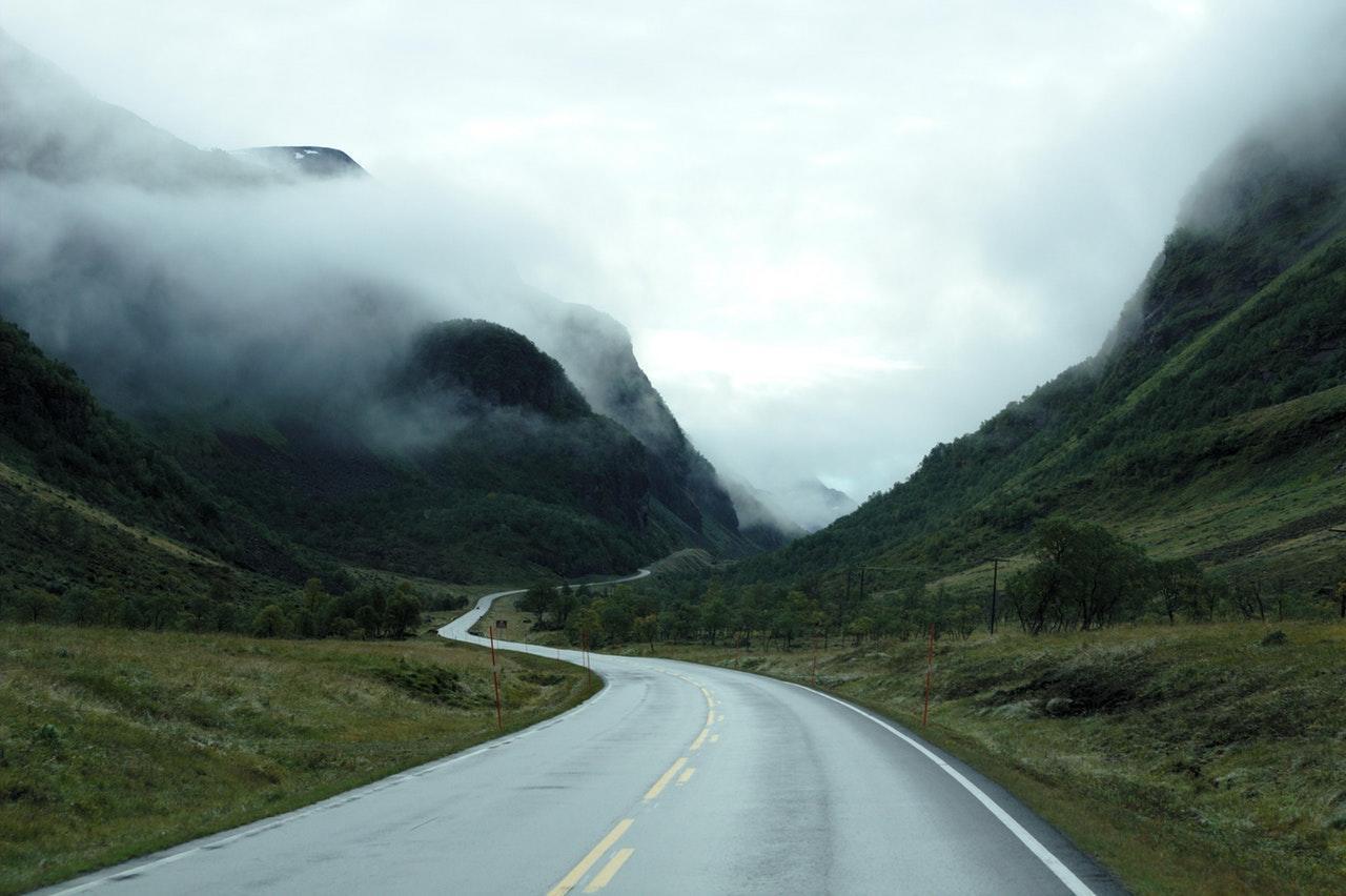 a winding road into the mountains and a foggy sky
