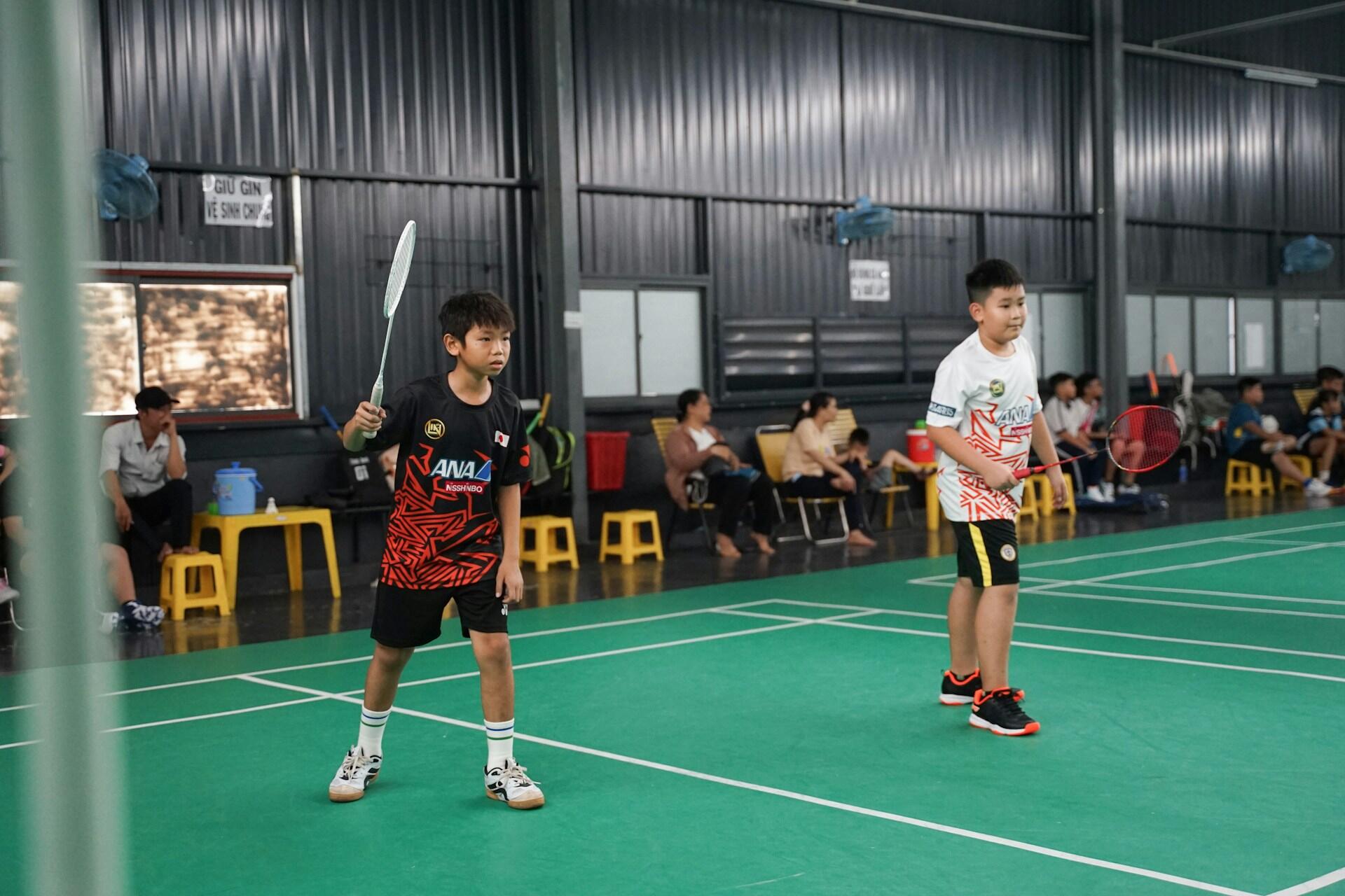 Two boys playing badminton on a green indoor court.