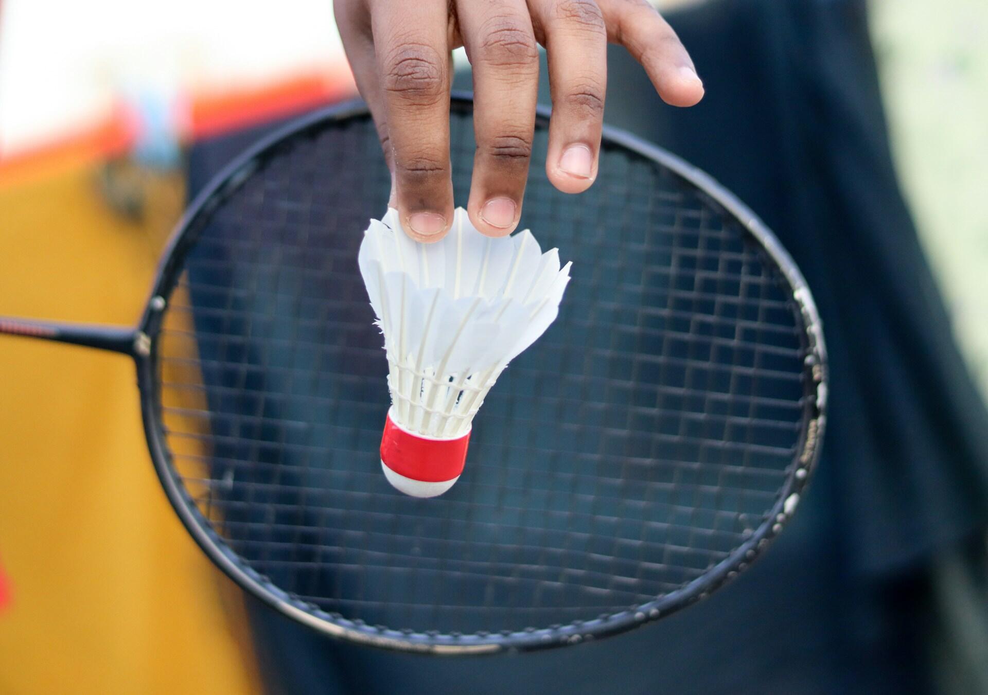 A person holding a shuttle in front of a badminton racket.