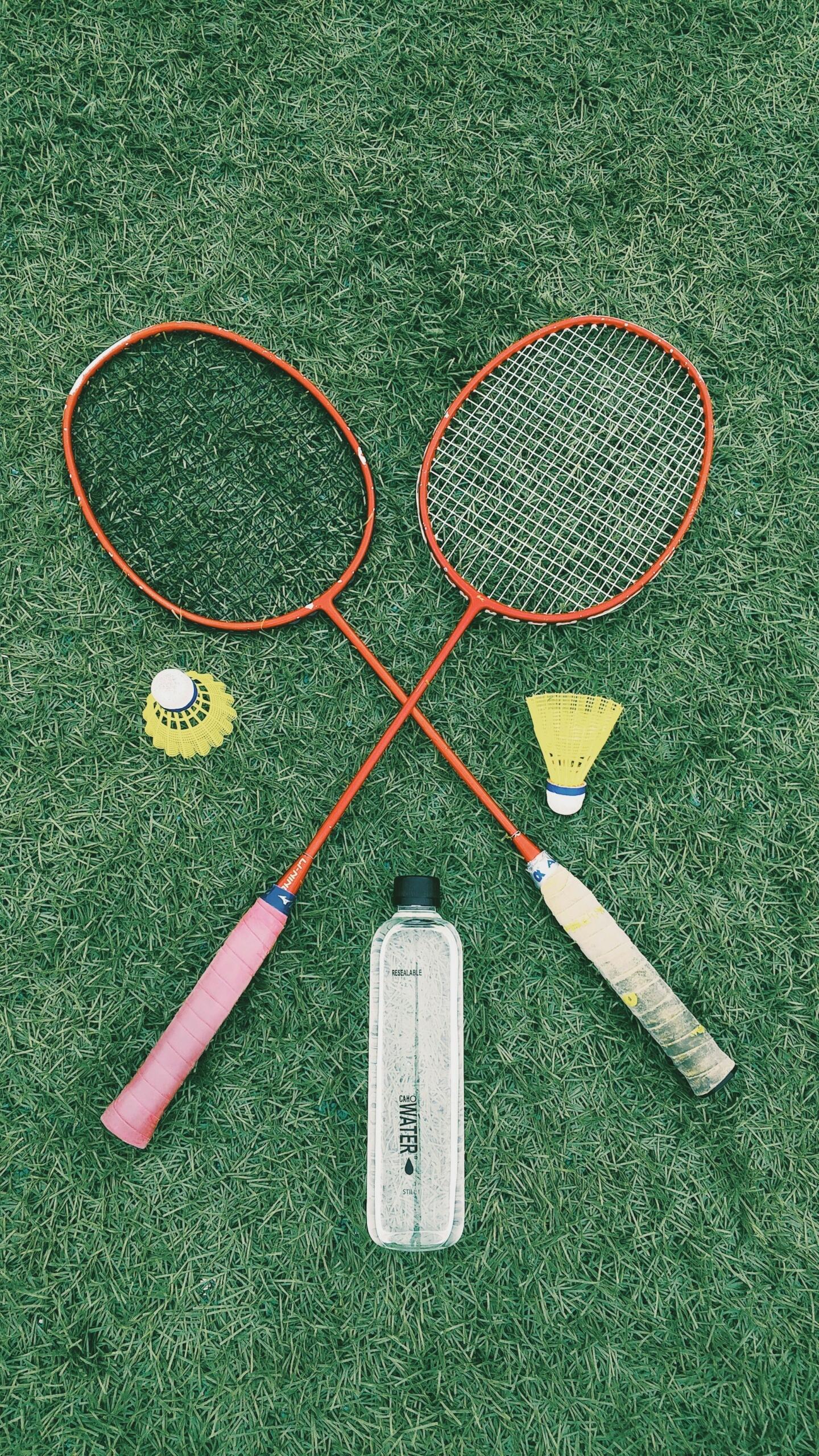 Two crossed badminton rackets and a water bottle on the grass.