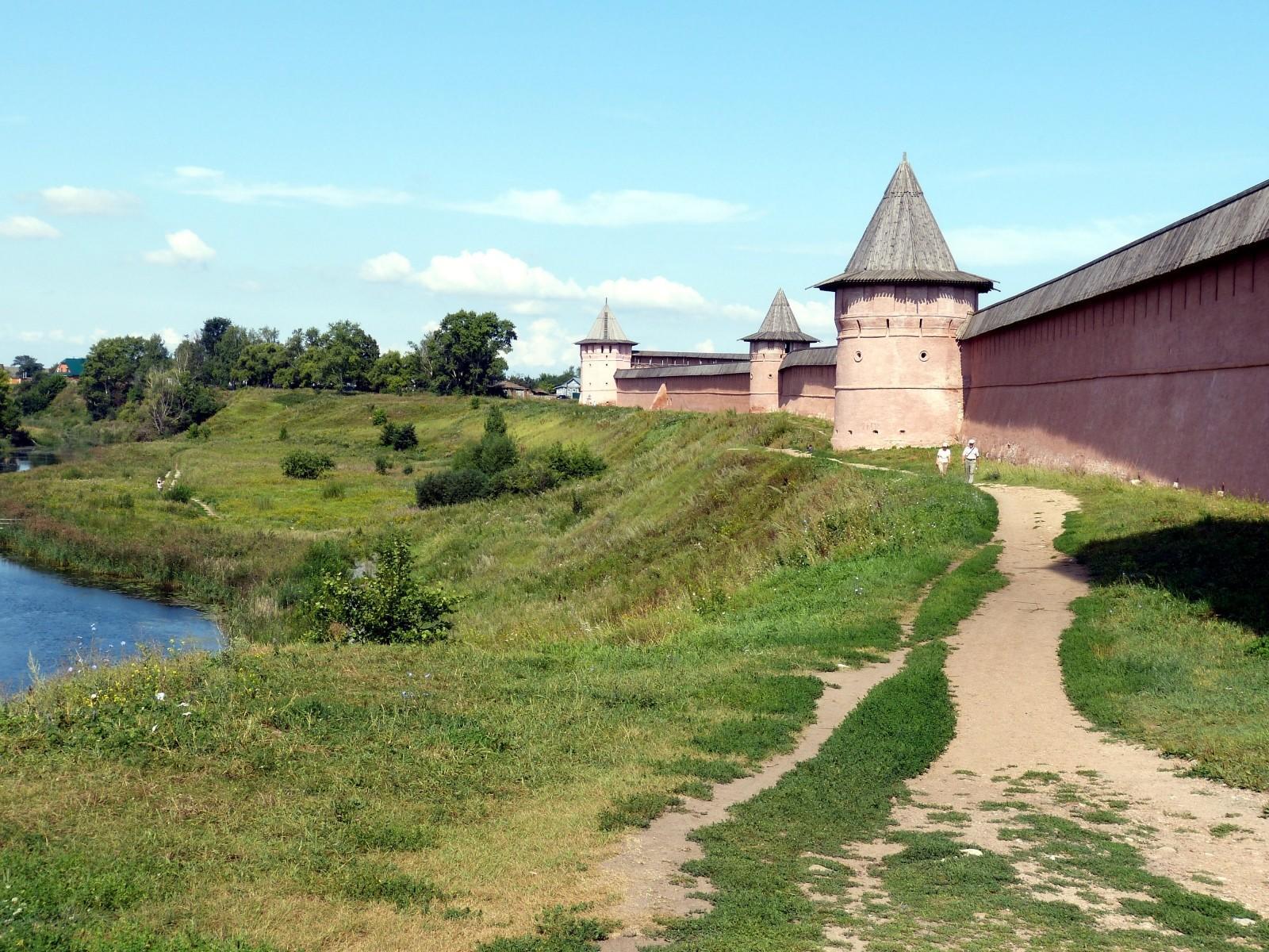 a walled fortress overlooking a lake and a field