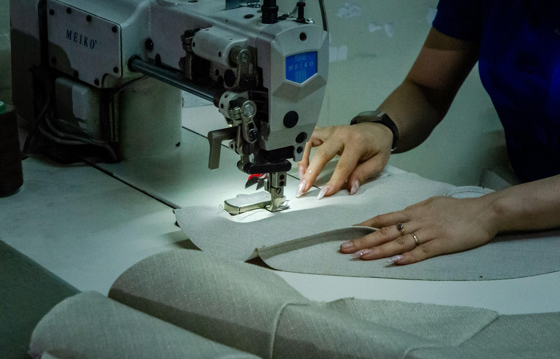 A close-up of a person sewing fabric on a sewing machine, focusing on hands, fabric pieces, and the sewing needle in action.