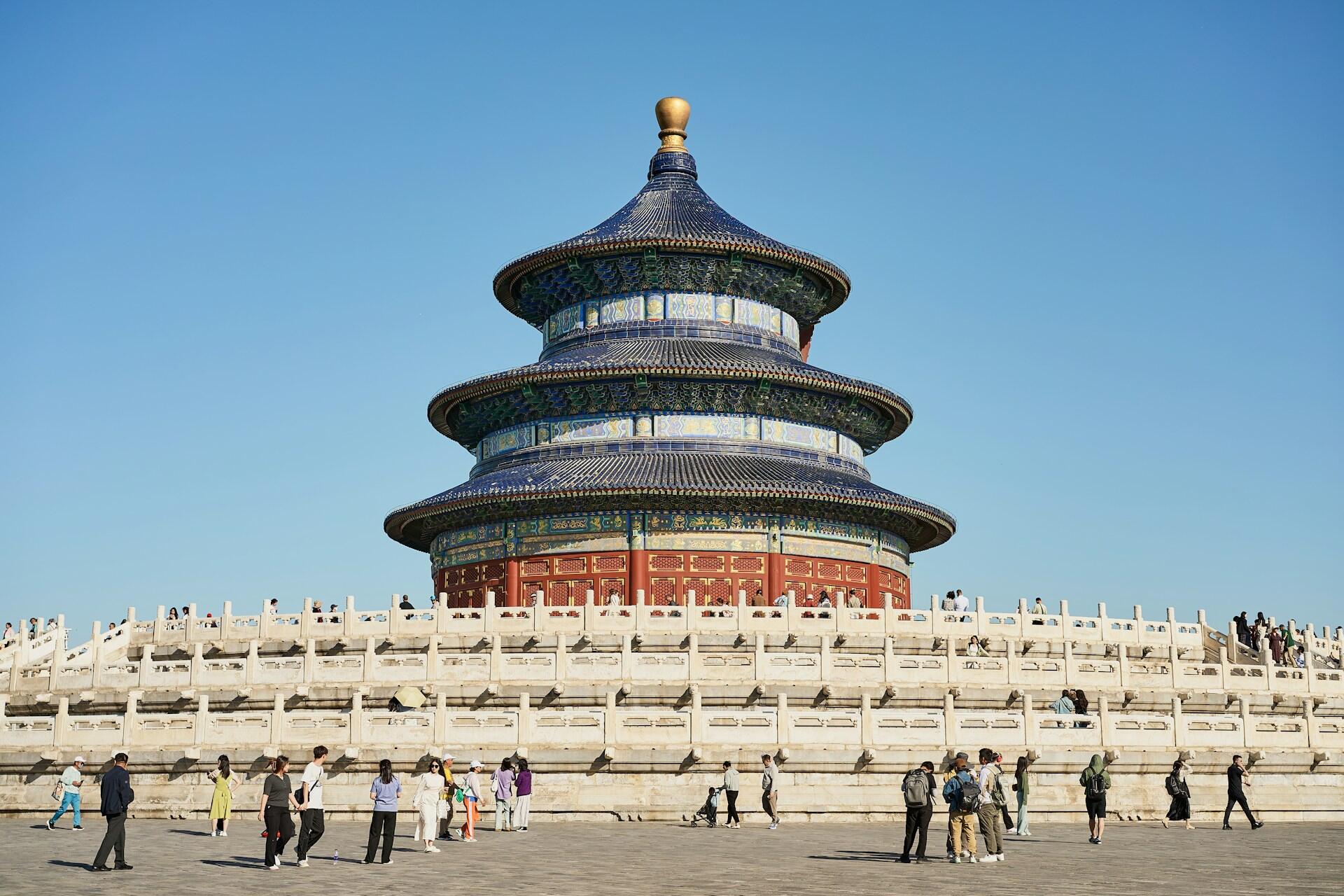 The Temple of Heaven in Beijing, featuring its iconic blue roof and surrounded by visitors against a clear blue sky.