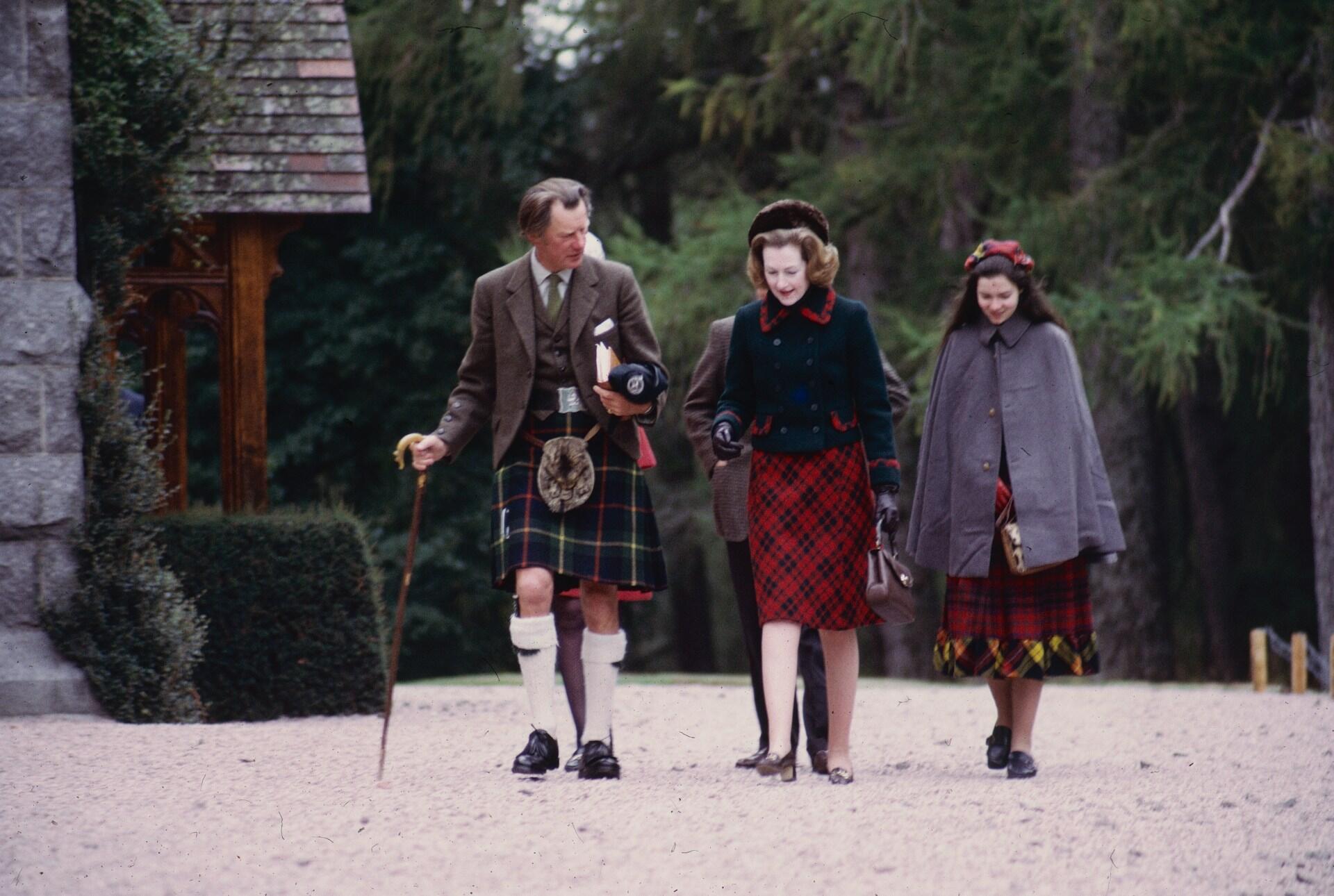 Three people wearing Scottish tartans on a gravel path.