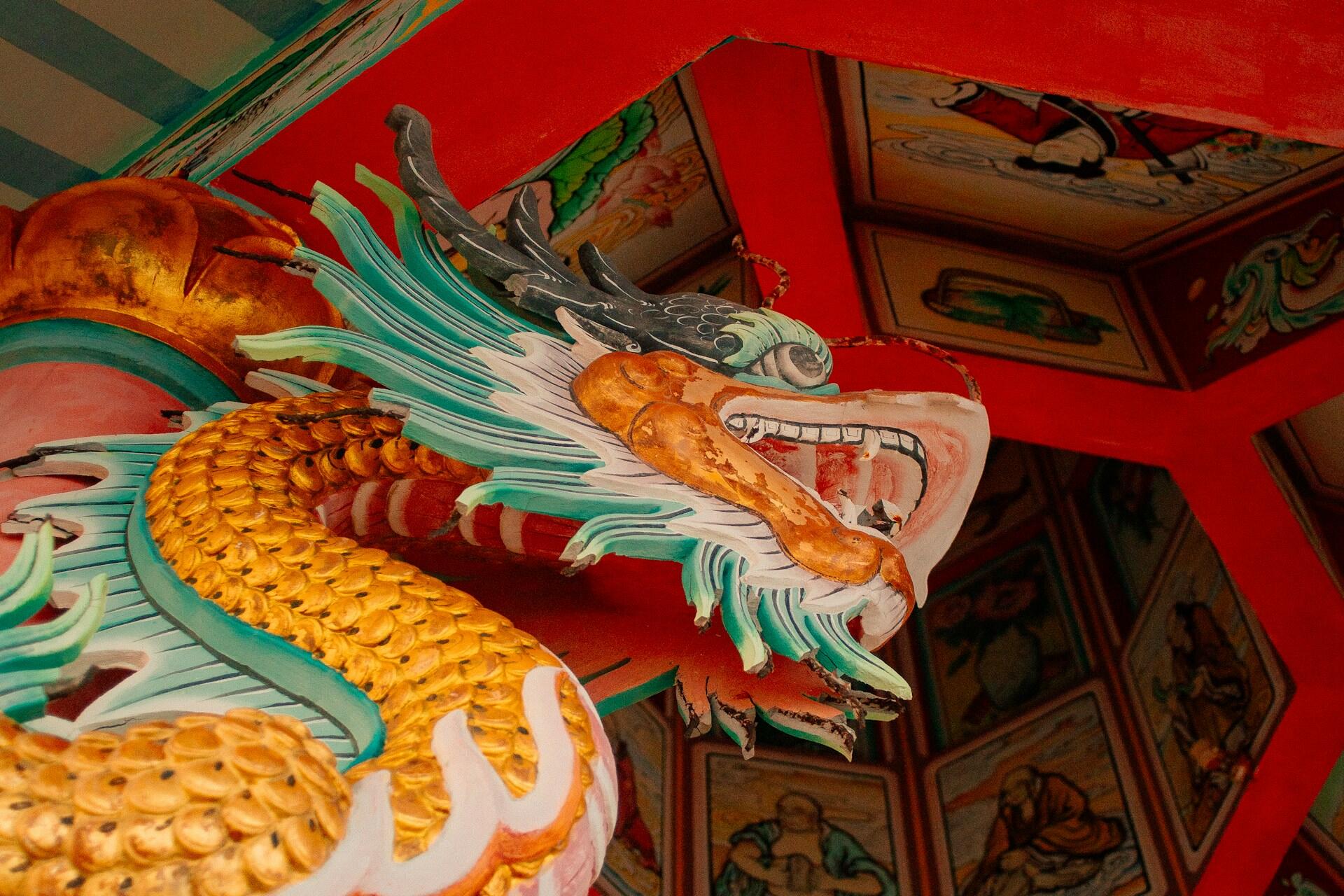 Close-up of a colorful dragon sculpture with intricate details, set against a vibrant red and patterned ceiling.