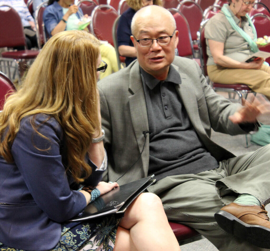 A writer talking to a woman while both are seated in an auditorium.