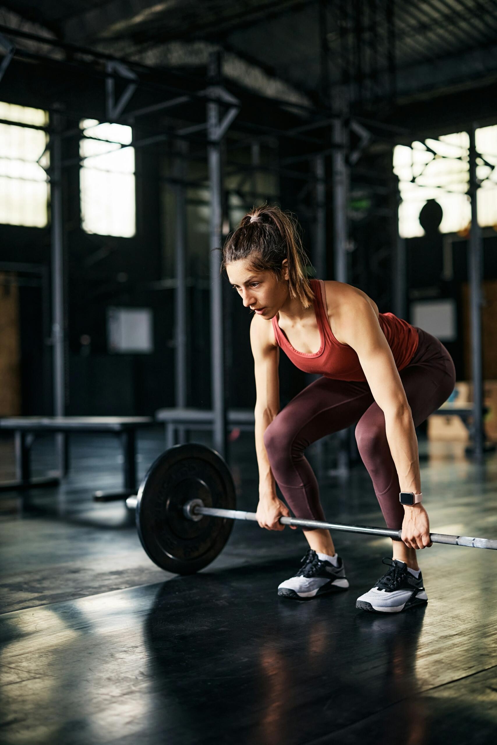 A person in activewear performs a deadlift with a barbell in a gym.