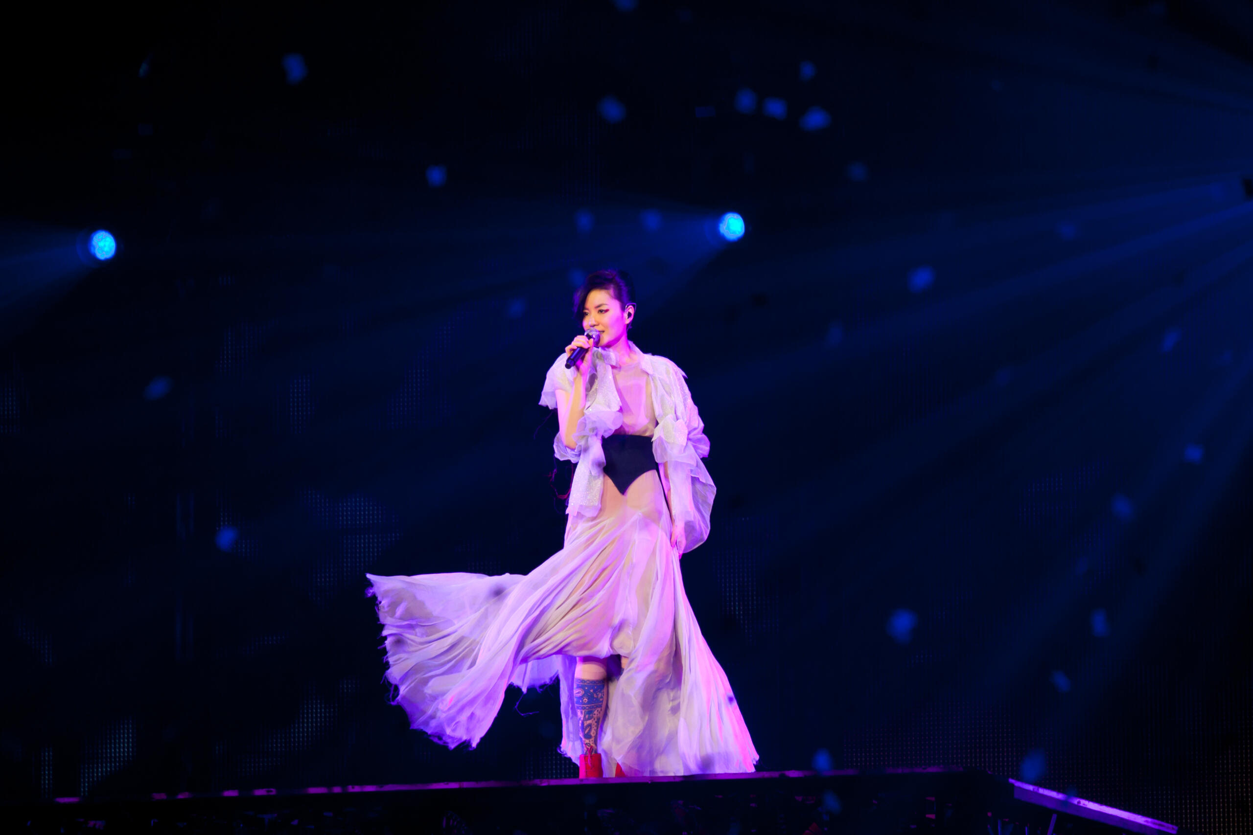 A Chinese pop artist performing in a white dress and stage lights.