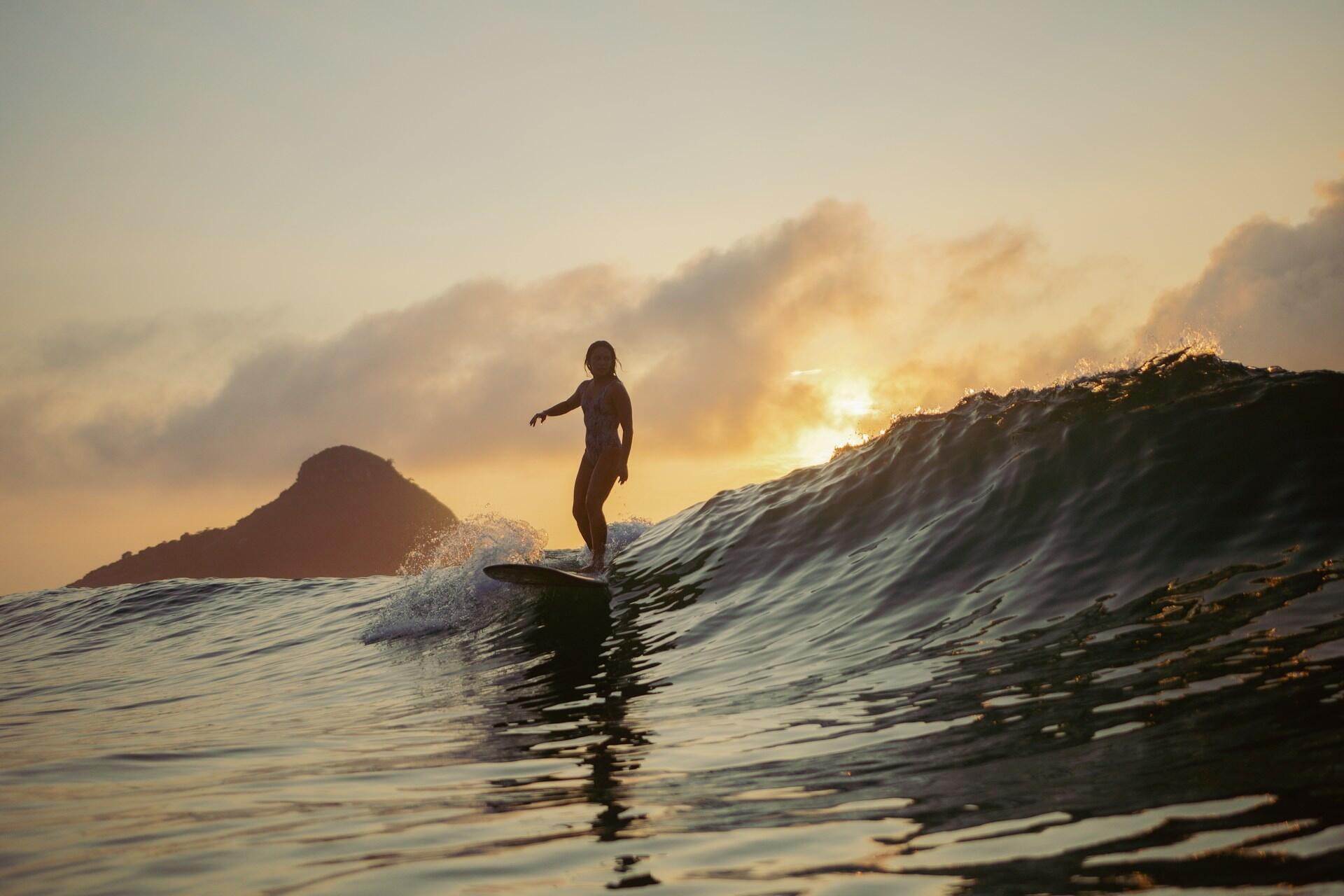 A person on a surfboard ahead of a cresting wave at sunset.