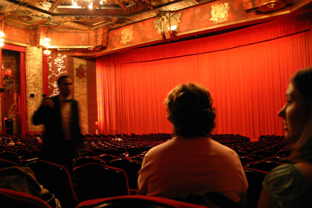 A red Chinese movie theater with red curtains, red seats and three people.