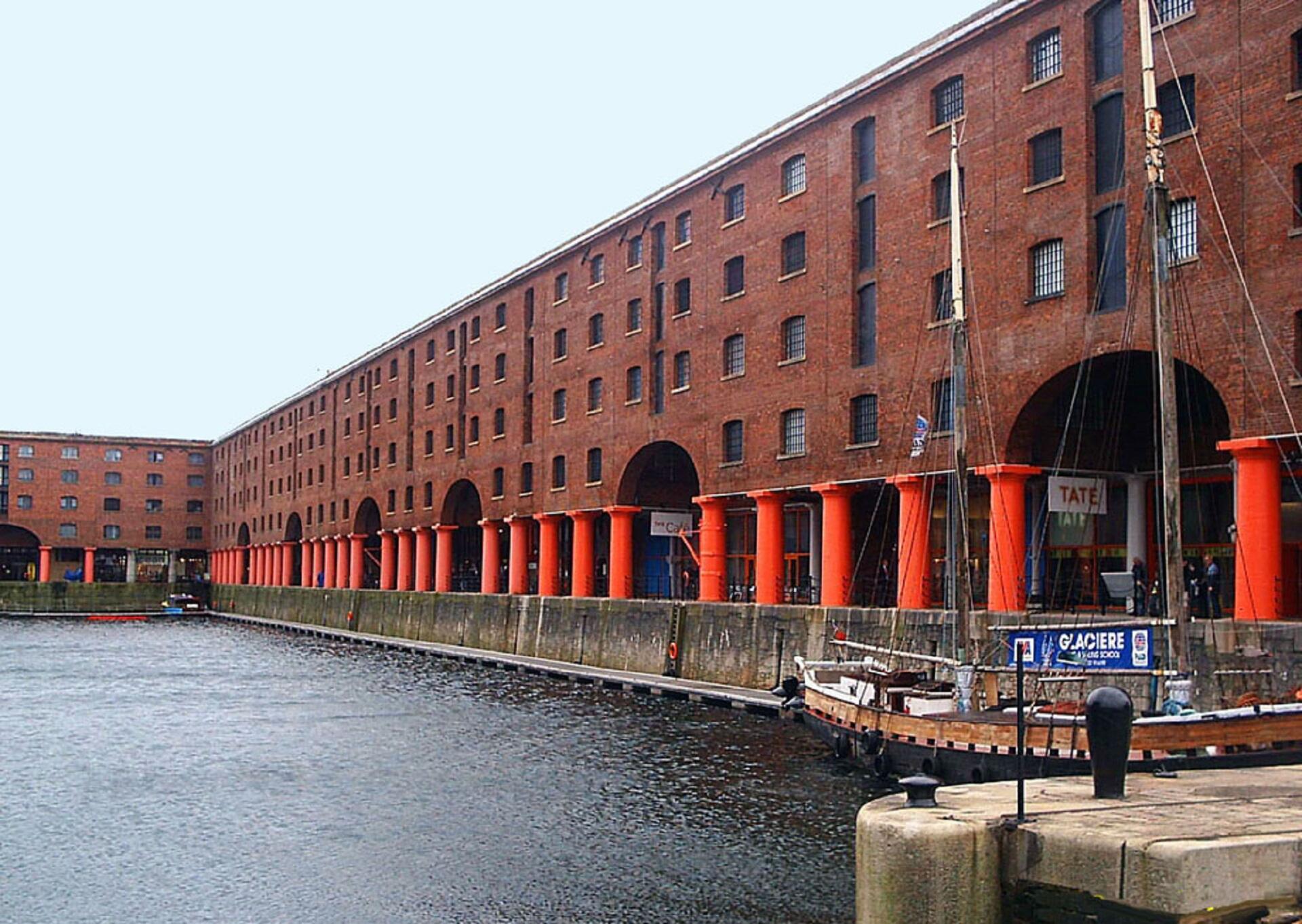 A long range of red brick buildings with bright neon orange pillars on the waterfront.