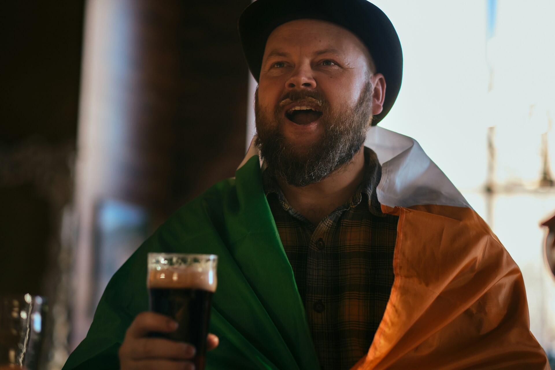 A man draped in an Irish flag holding a Guinness
