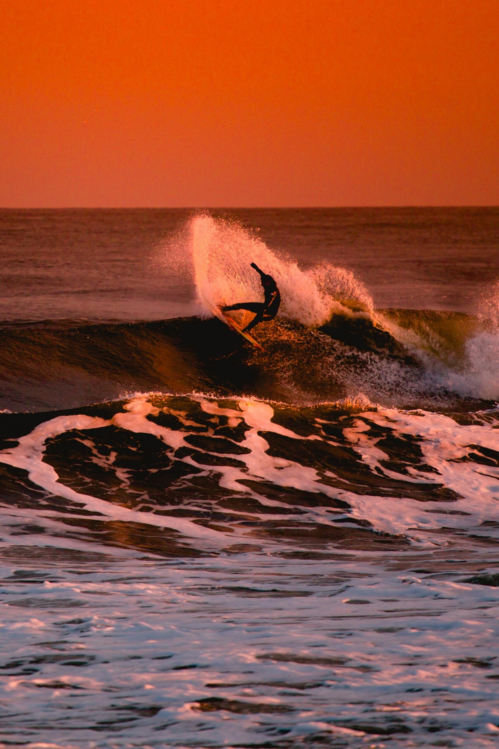 A surfer riding a cresting wave in waning light.