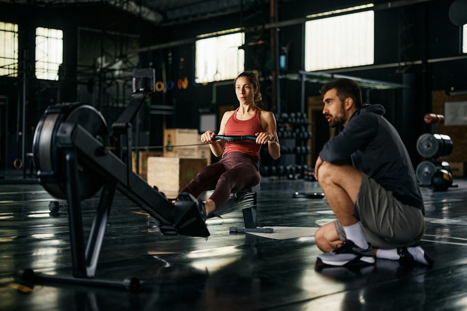 A woman works a rowing machine while a coach looks on.