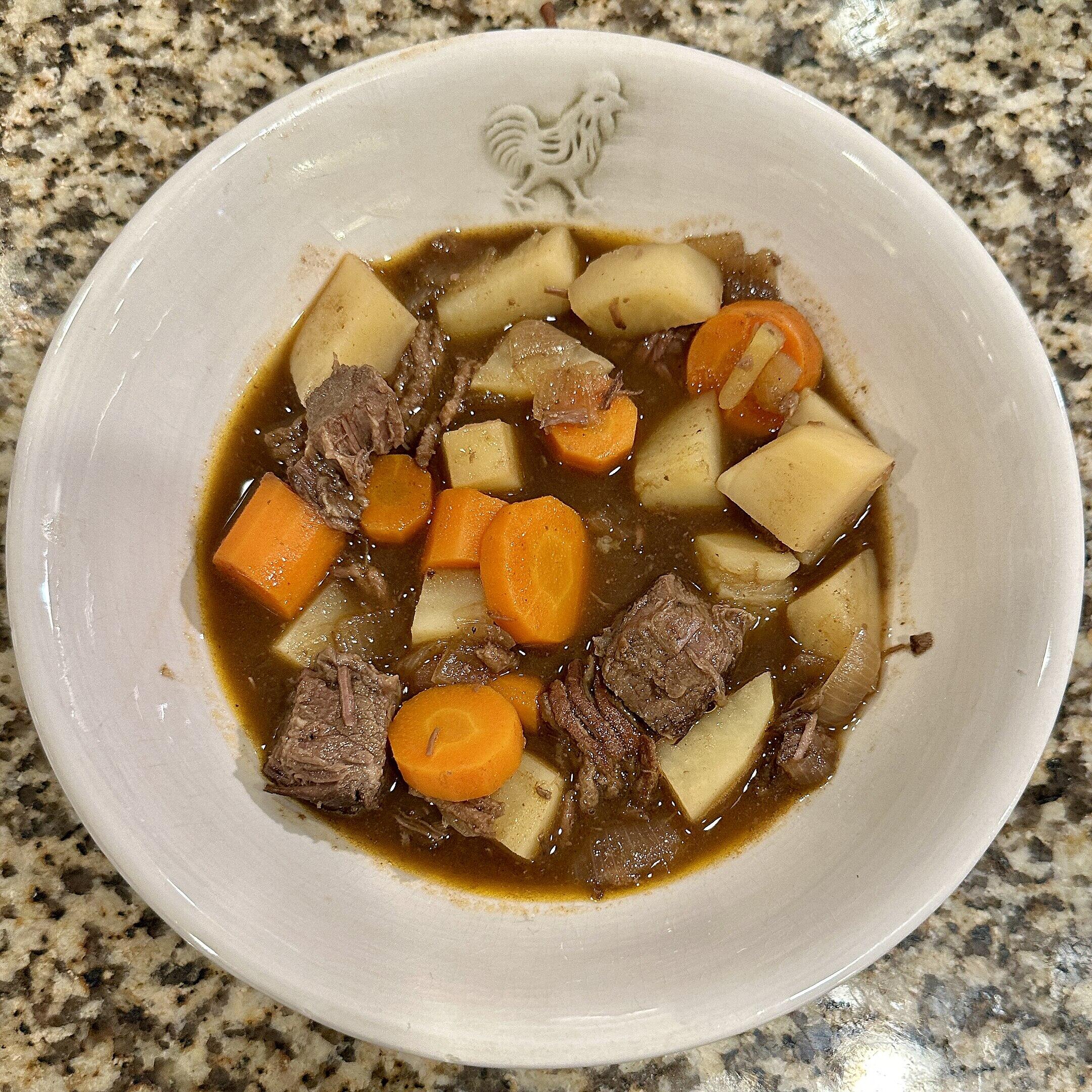 A bowl of soup with meat, potato and carrots.