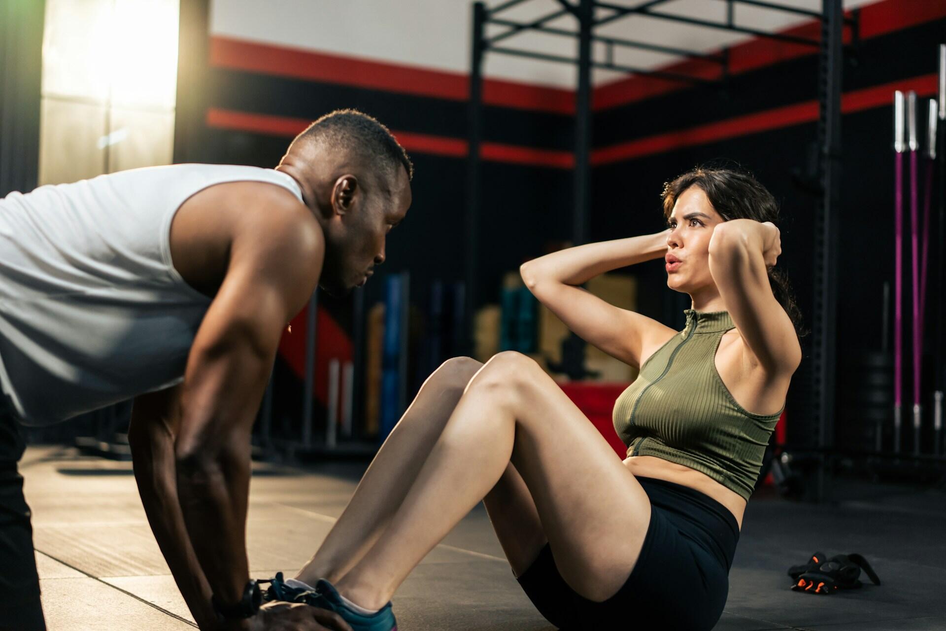 A woman does sit-ups while a coach holds her feet.