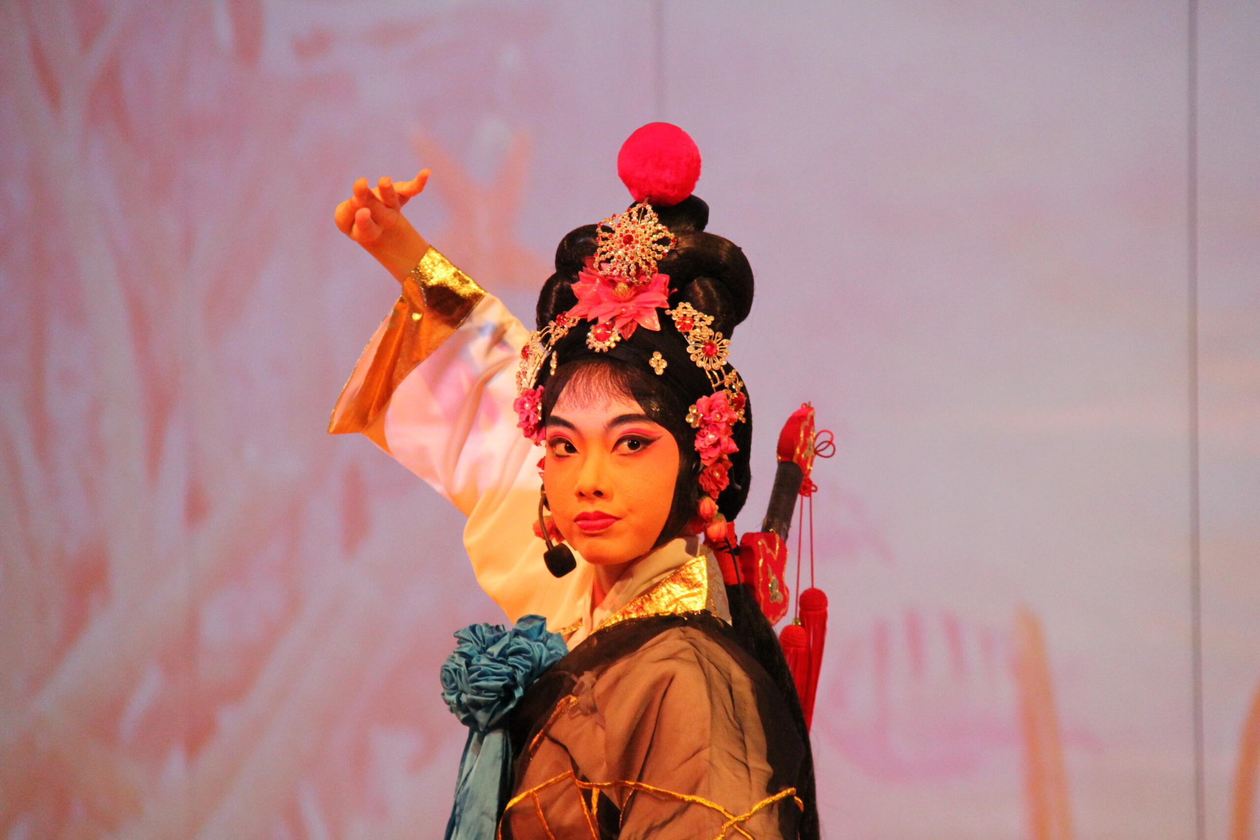 Opera artist doing a performance with make-up and wearing a traditional costume in front of a pink background.