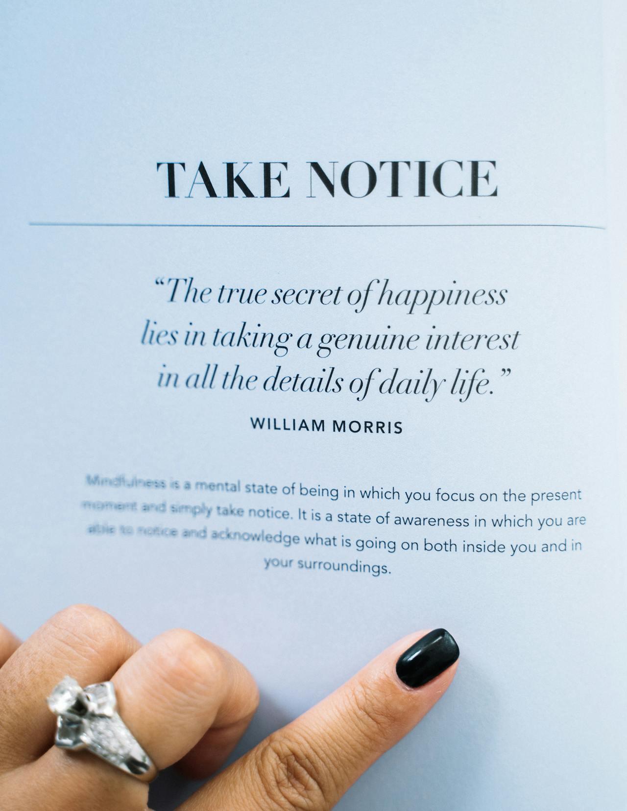 A hand with a silver ring points to an open book page featuring a quote about mindfulness and happiness by William Morris.