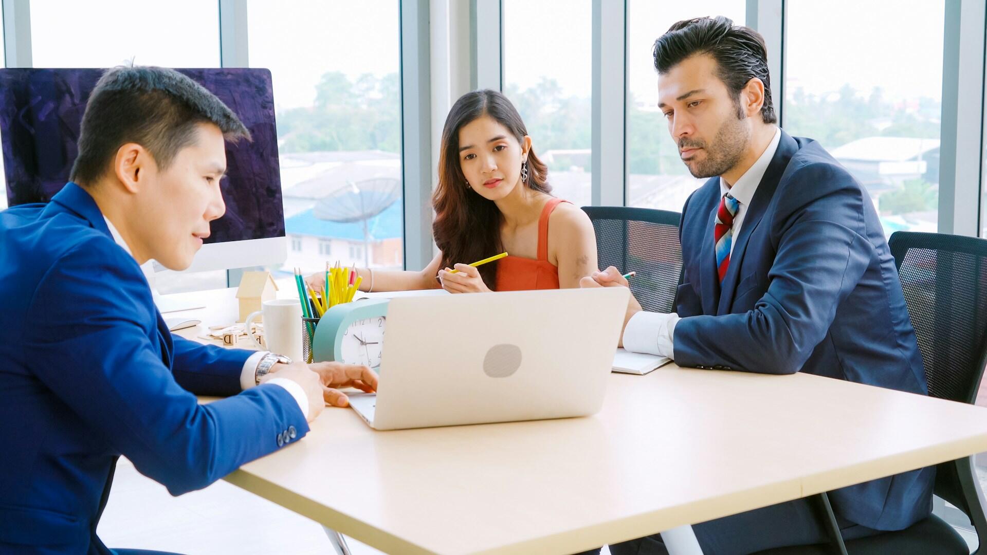 Three people at a table focused on a computer. 