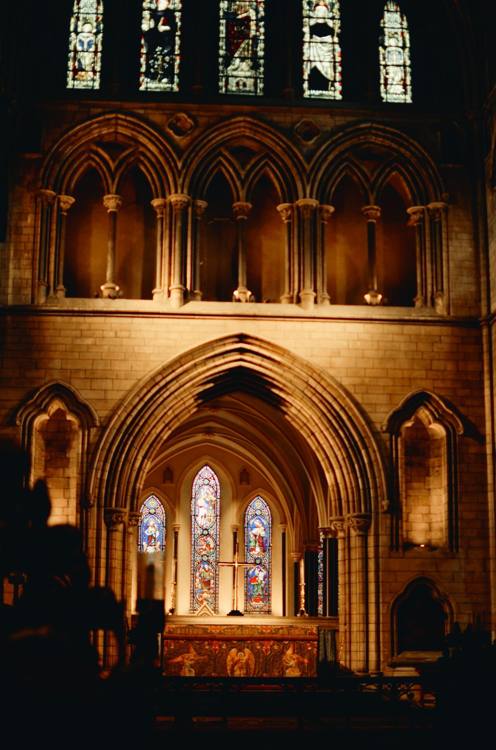 Interior of a church featuring arched architecture, stained glass windows, and an altar illuminated by soft lighting.