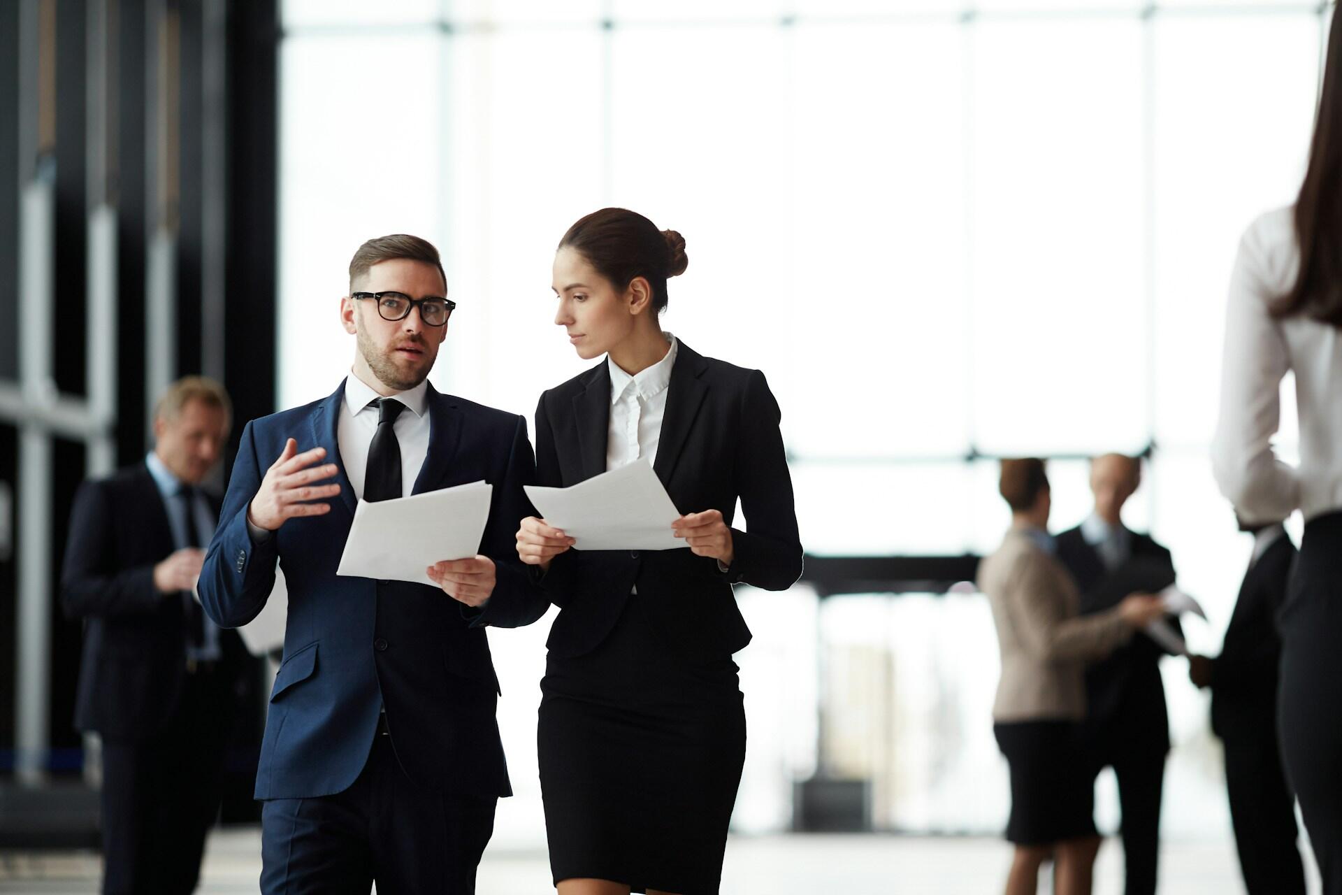 People in business suits holding papers and walking while talking.