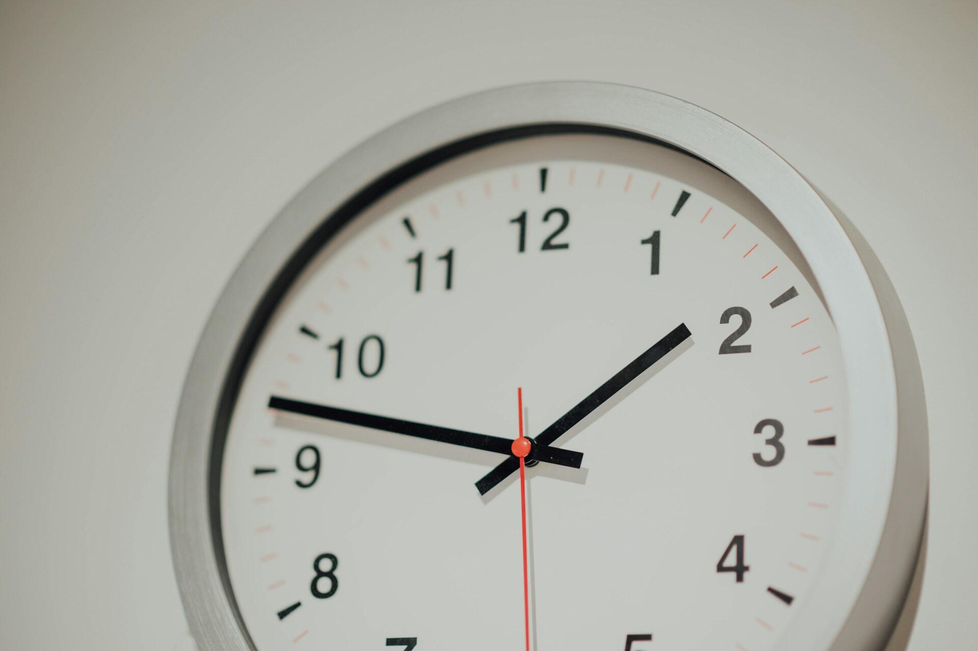 Close-up of a wall clock showing the time as 10:10, with a silver frame, black hour and minute hands, and a red second hand.