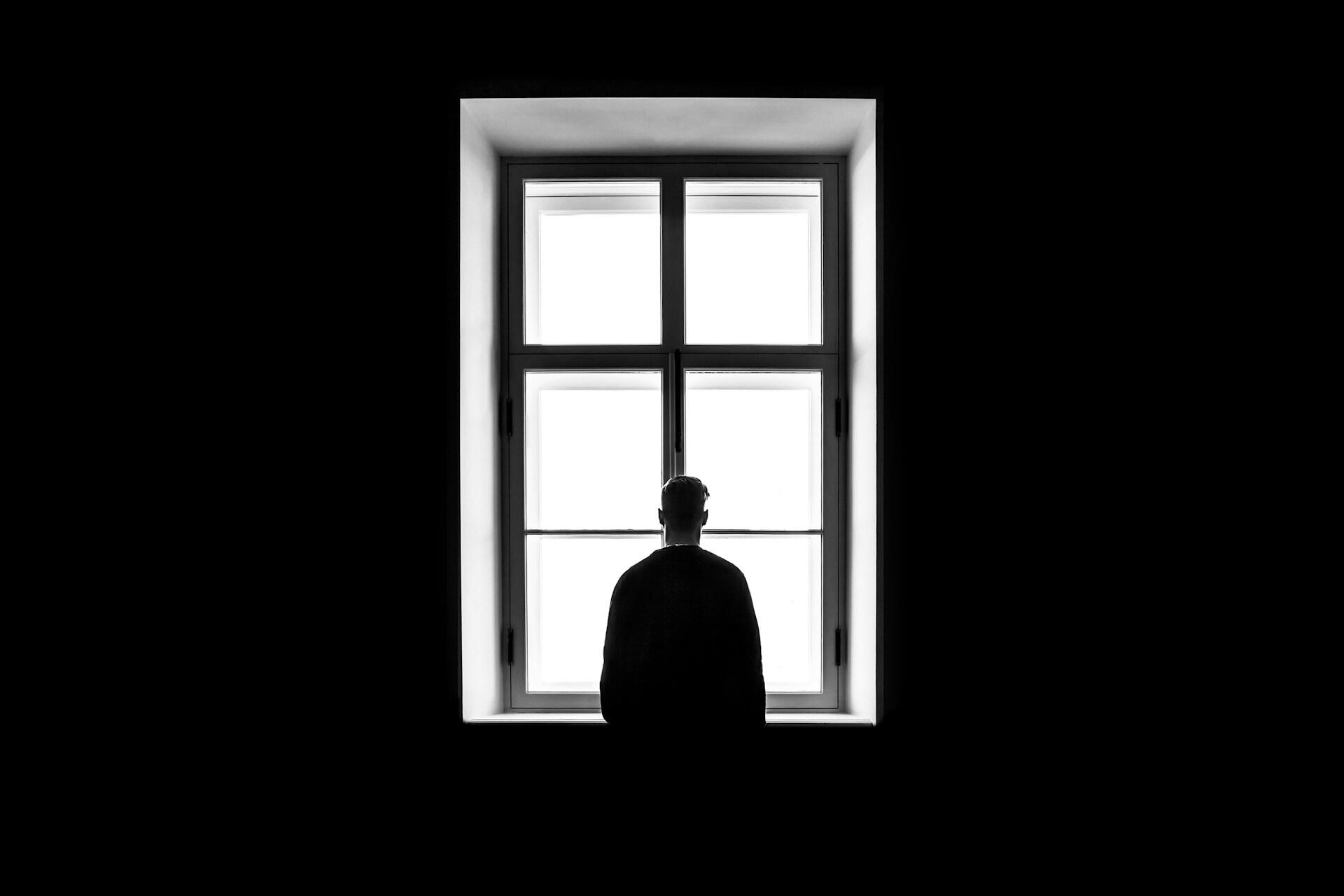 A person stands in front of a window in a dark room.