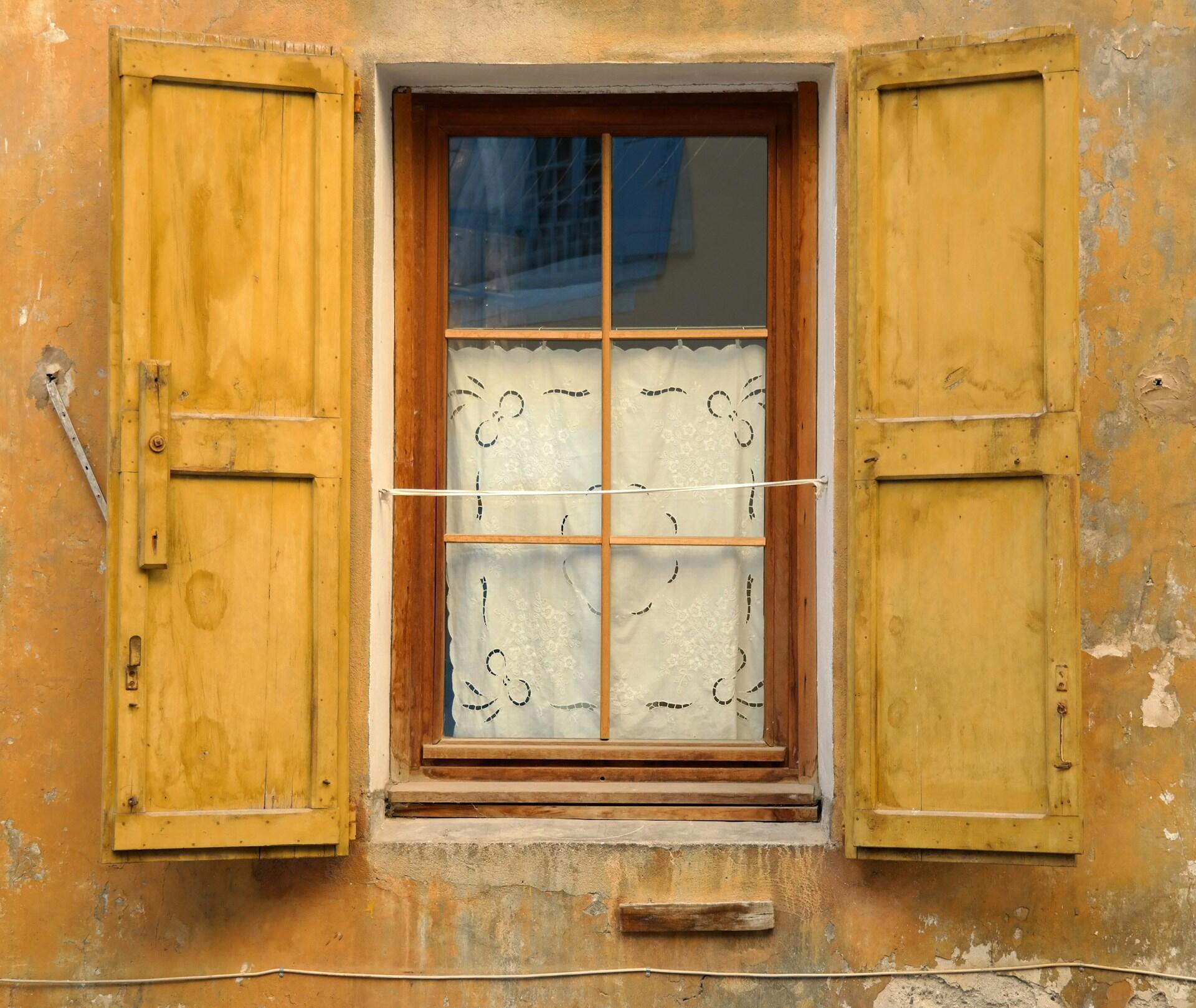 A window with a white curtain and yellow shutters.